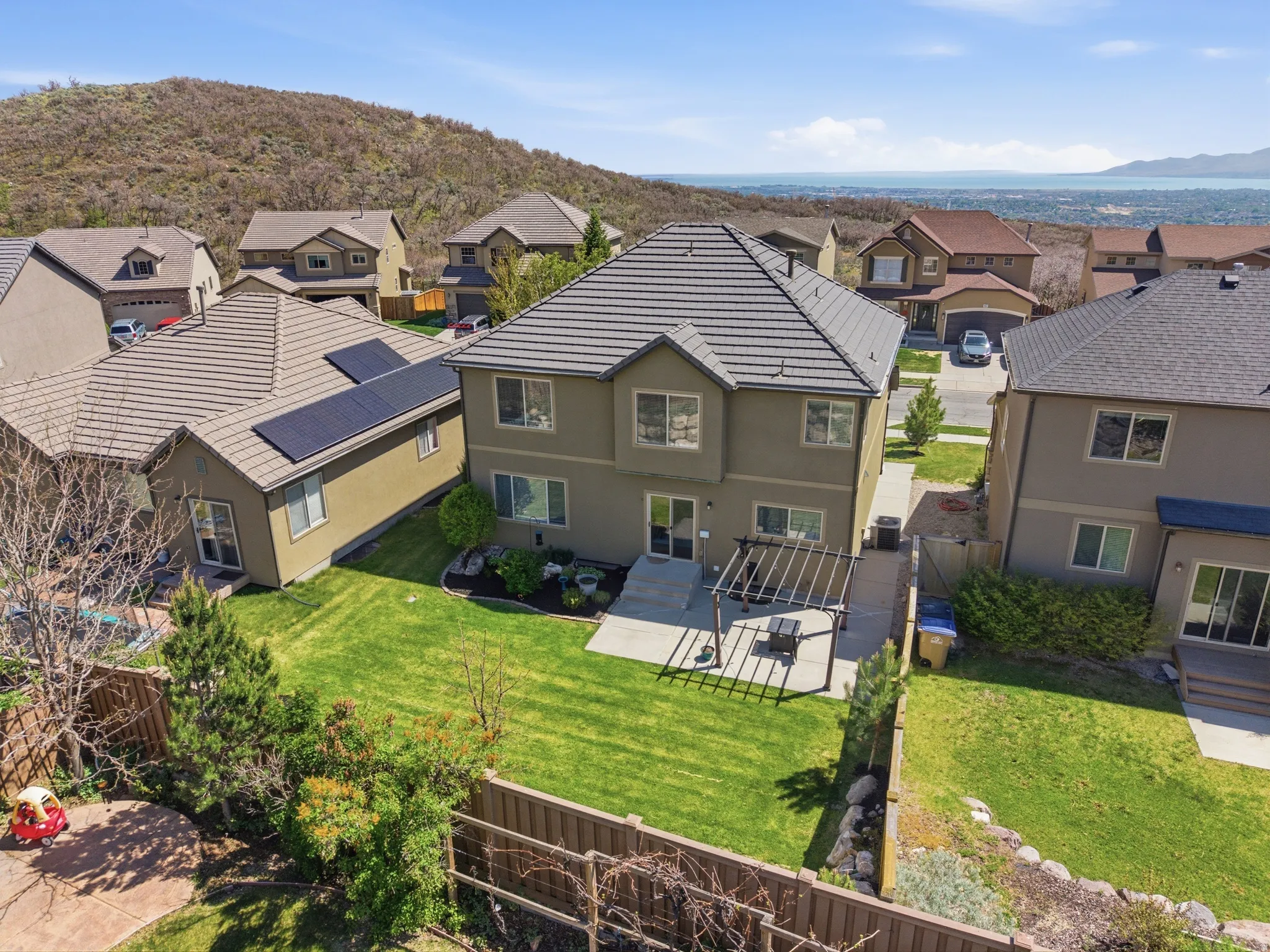 Rear exterior featuring a spacious lawn, extended patio with a pergola, and mature landscaping