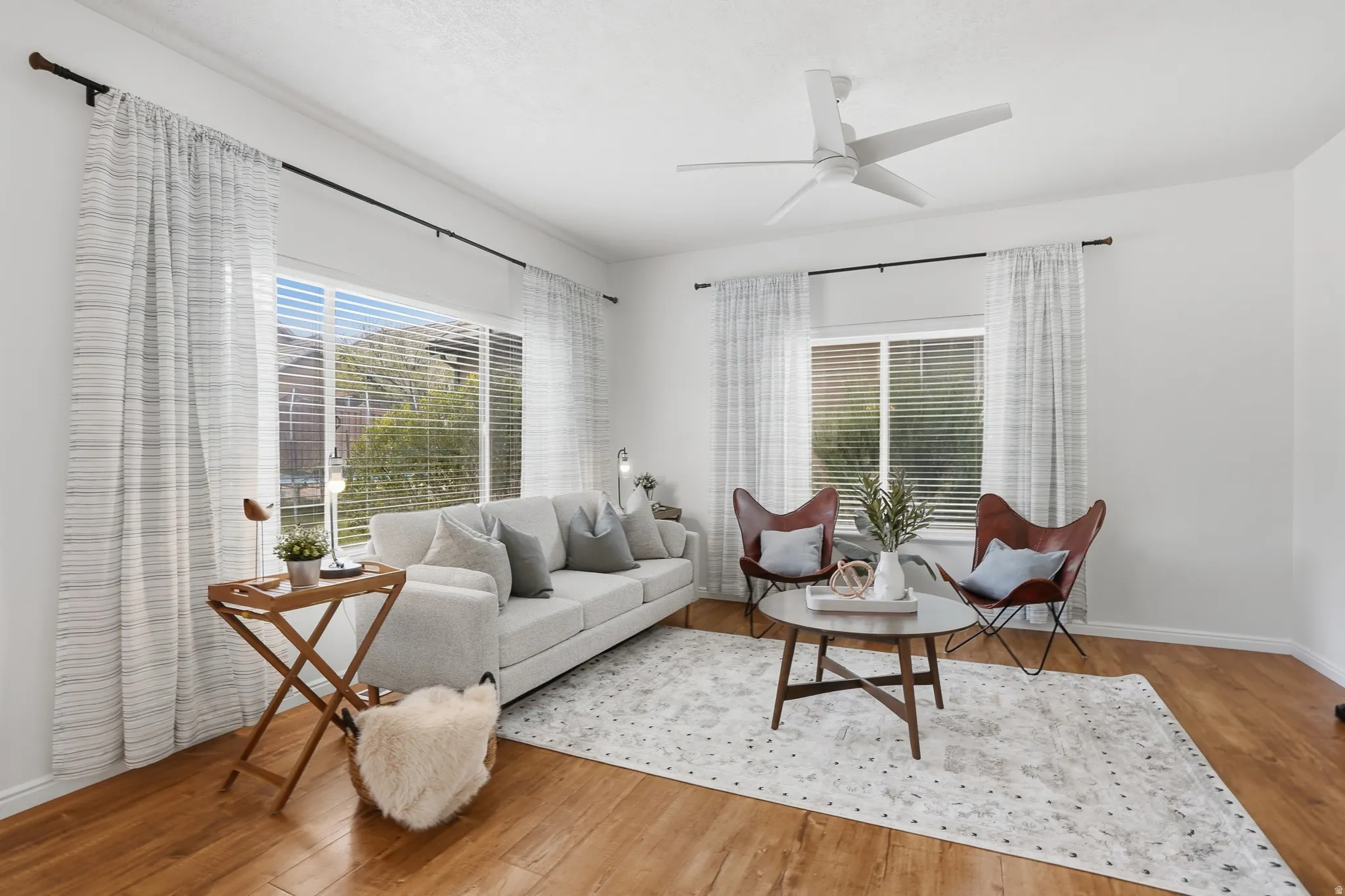 Bright living space featuring abundant natural light, wood-finish flooring, a contemporary ceiling fan, white walls, and horizontal window blinds