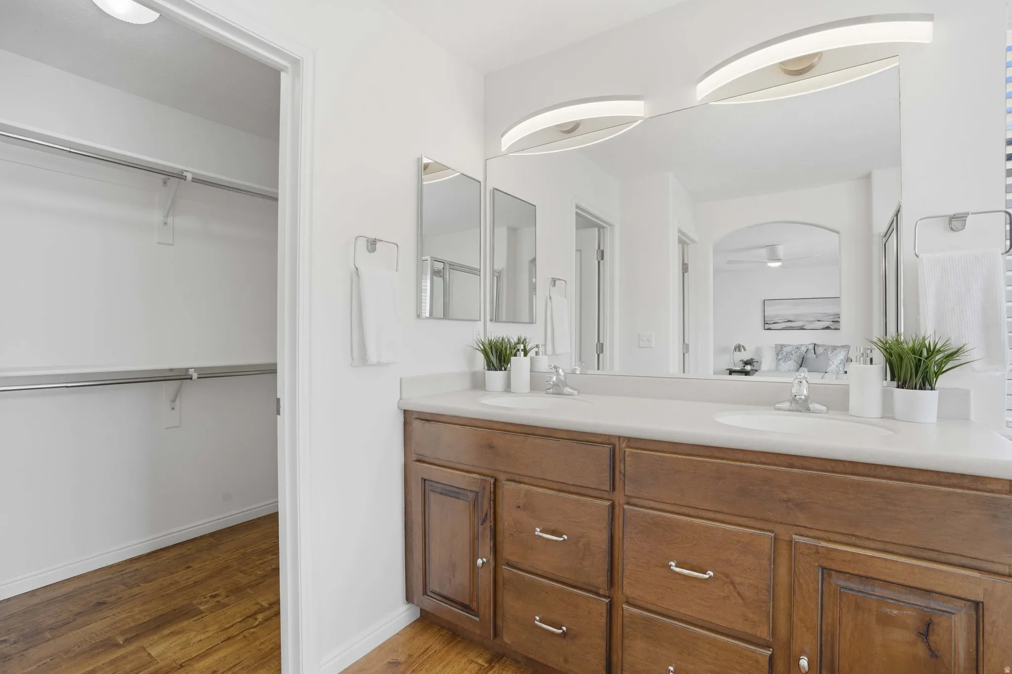 Dual sink vanity with wood-finish cabinetry and chrome hardware, featuring a large mirror with integrated lighting