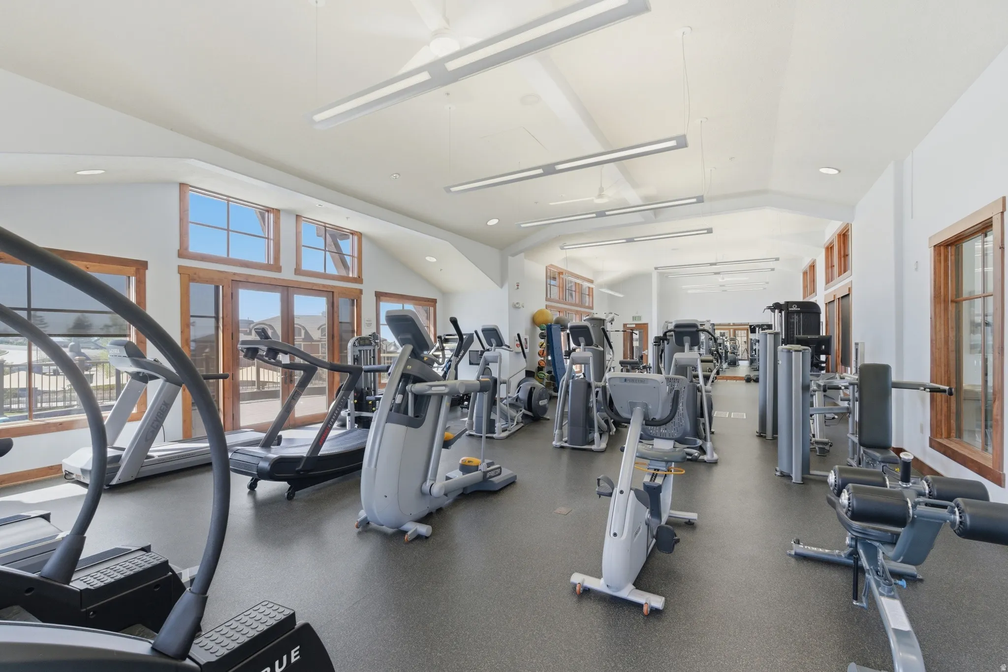 Spacious fitness center featuring a high vaulted ceiling, exposed wood-frame windows, and recessed lighting