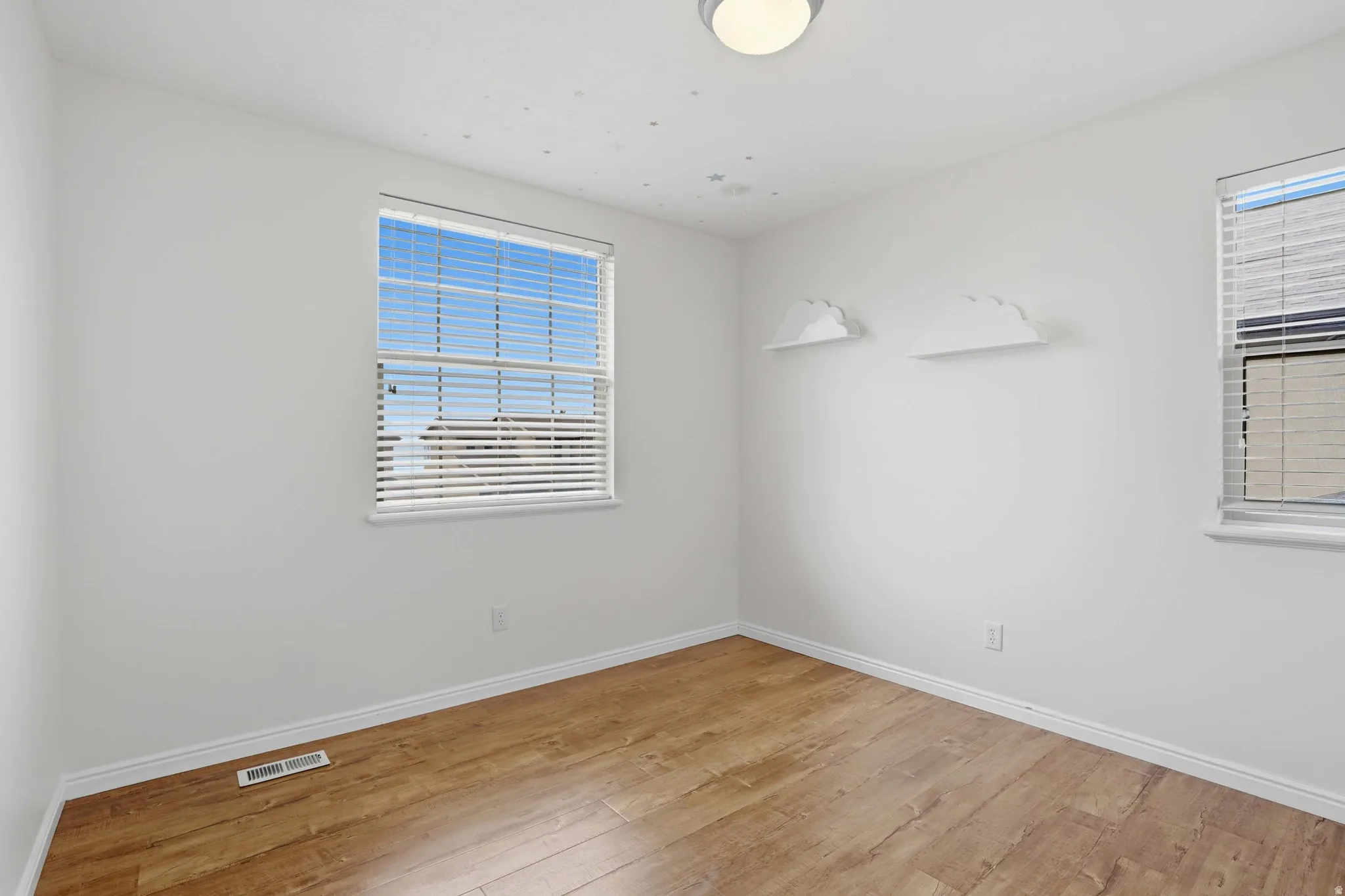 Bright room featuring two windows with blinds, wood-finish flooring, white baseboards, and a flush-mount ceiling light