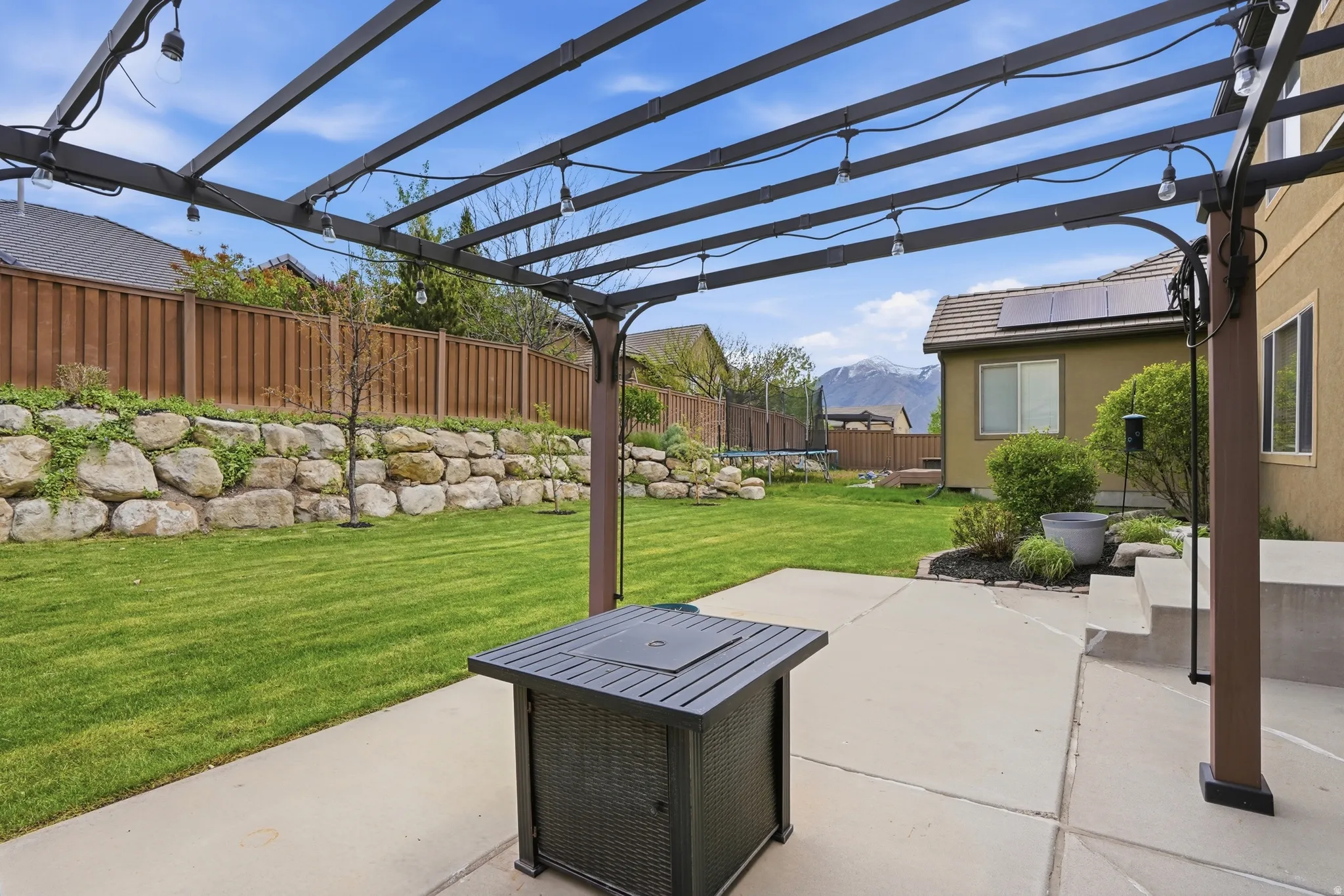 Patio featuring a dark-toned pergola with string lighting, a concrete surface, and steps leading from the property