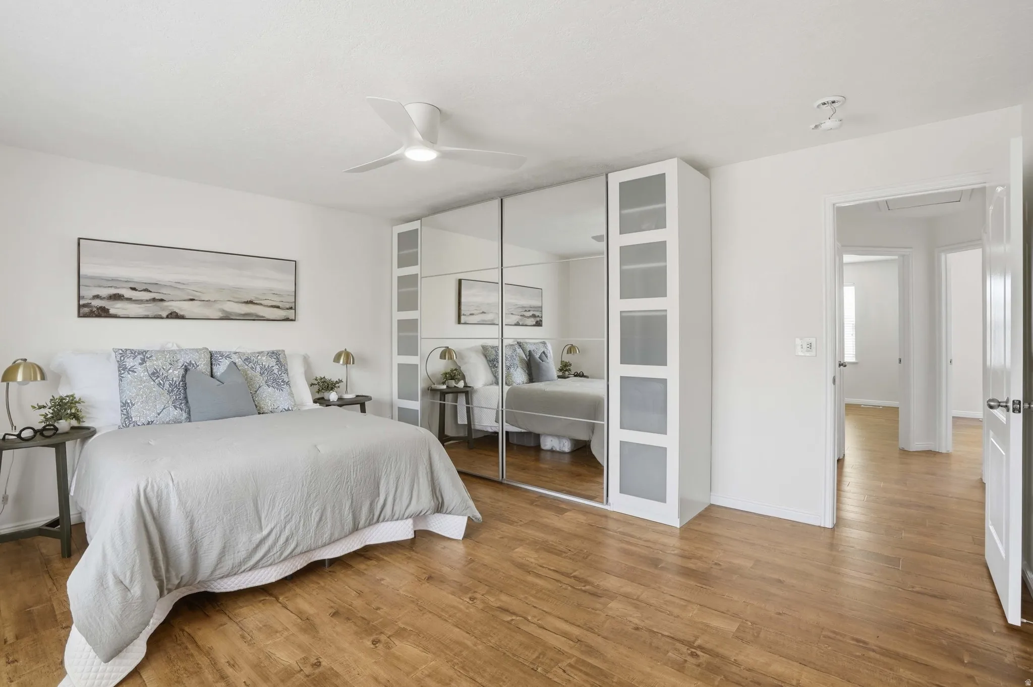 Spacious room featuring wood-finish flooring, white walls, and a ceiling fan