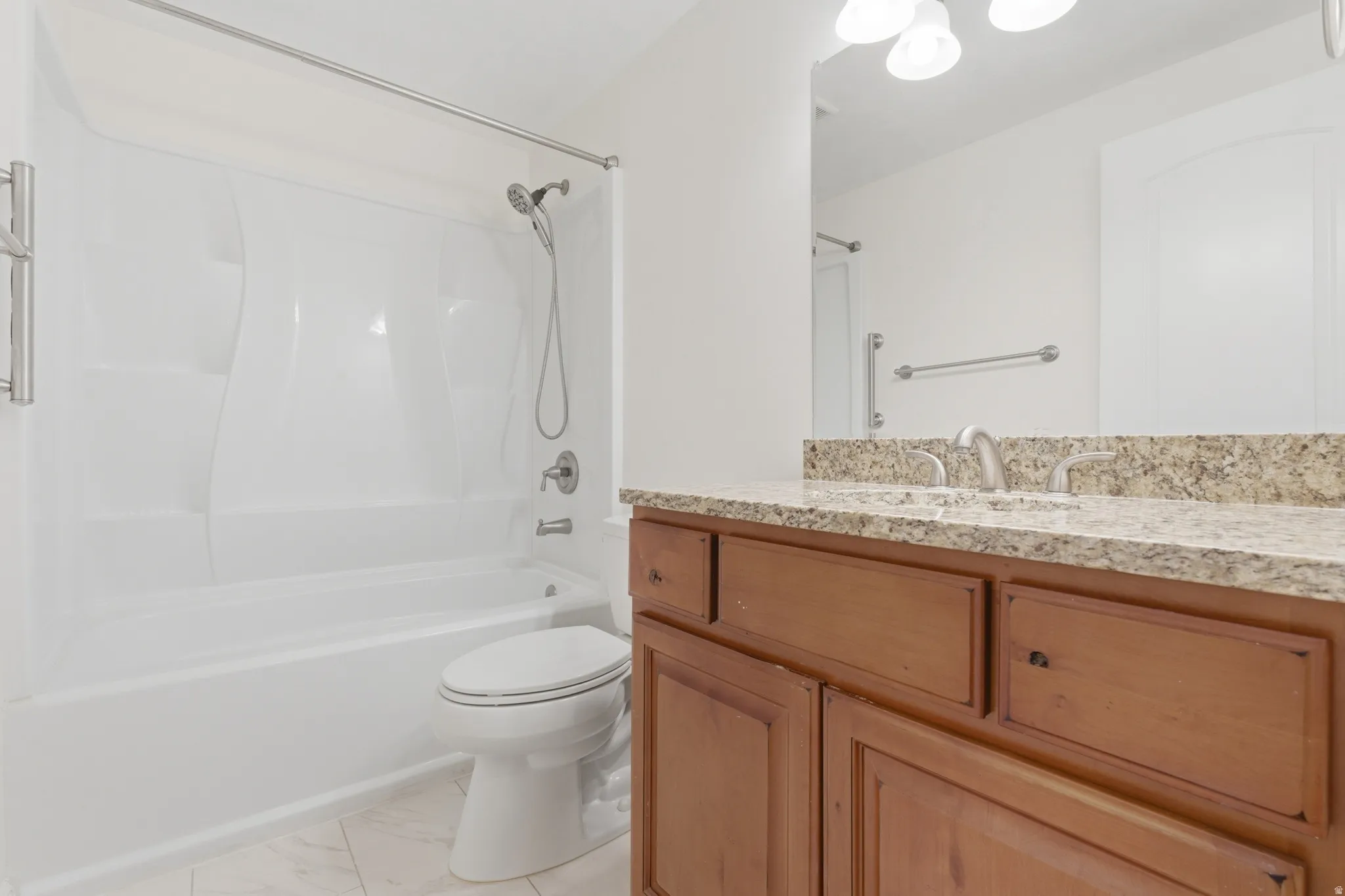 Bathroom featuring a combination shower/tub with a handheld showerhead, a toilet, a double vanity with a granite-style countertop, and wood-finish cabinetry