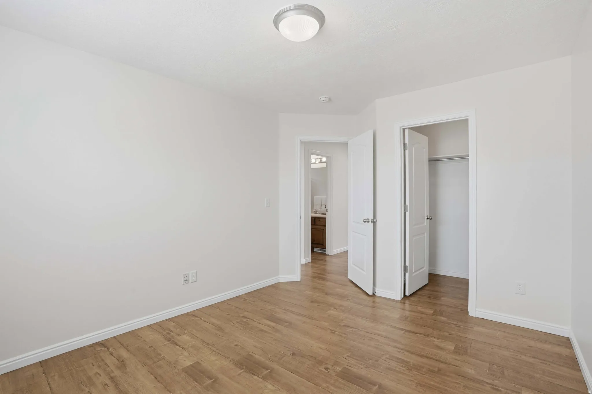 Spacious interior room featuring wood-finish flooring, white baseboards, and a neutral wall color