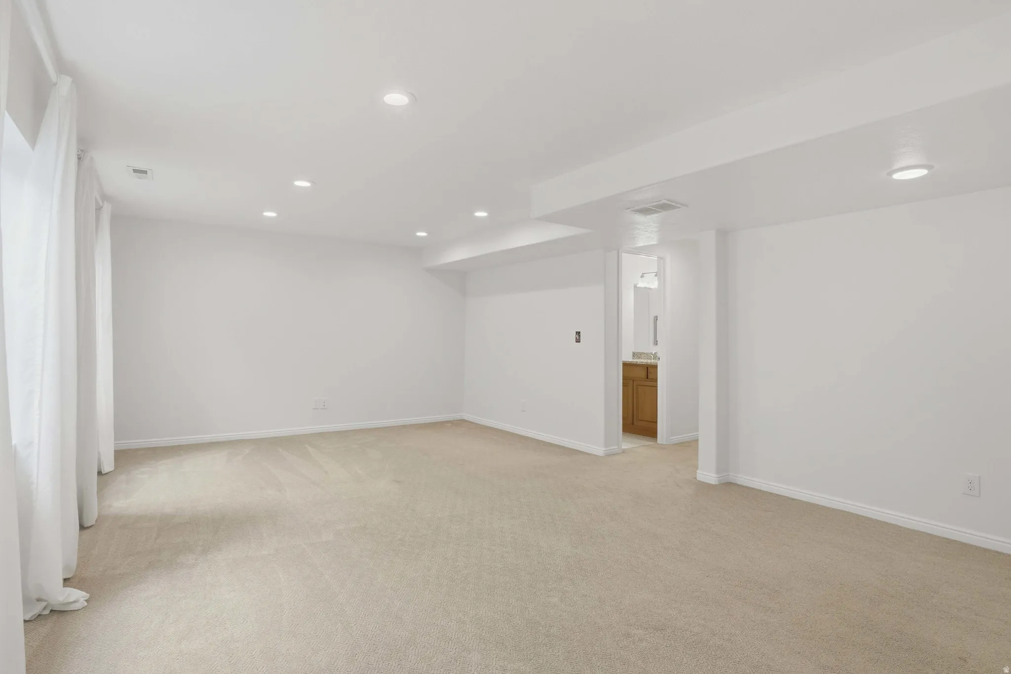 Spacious carpeted room featuring recessed lighting and white drapery