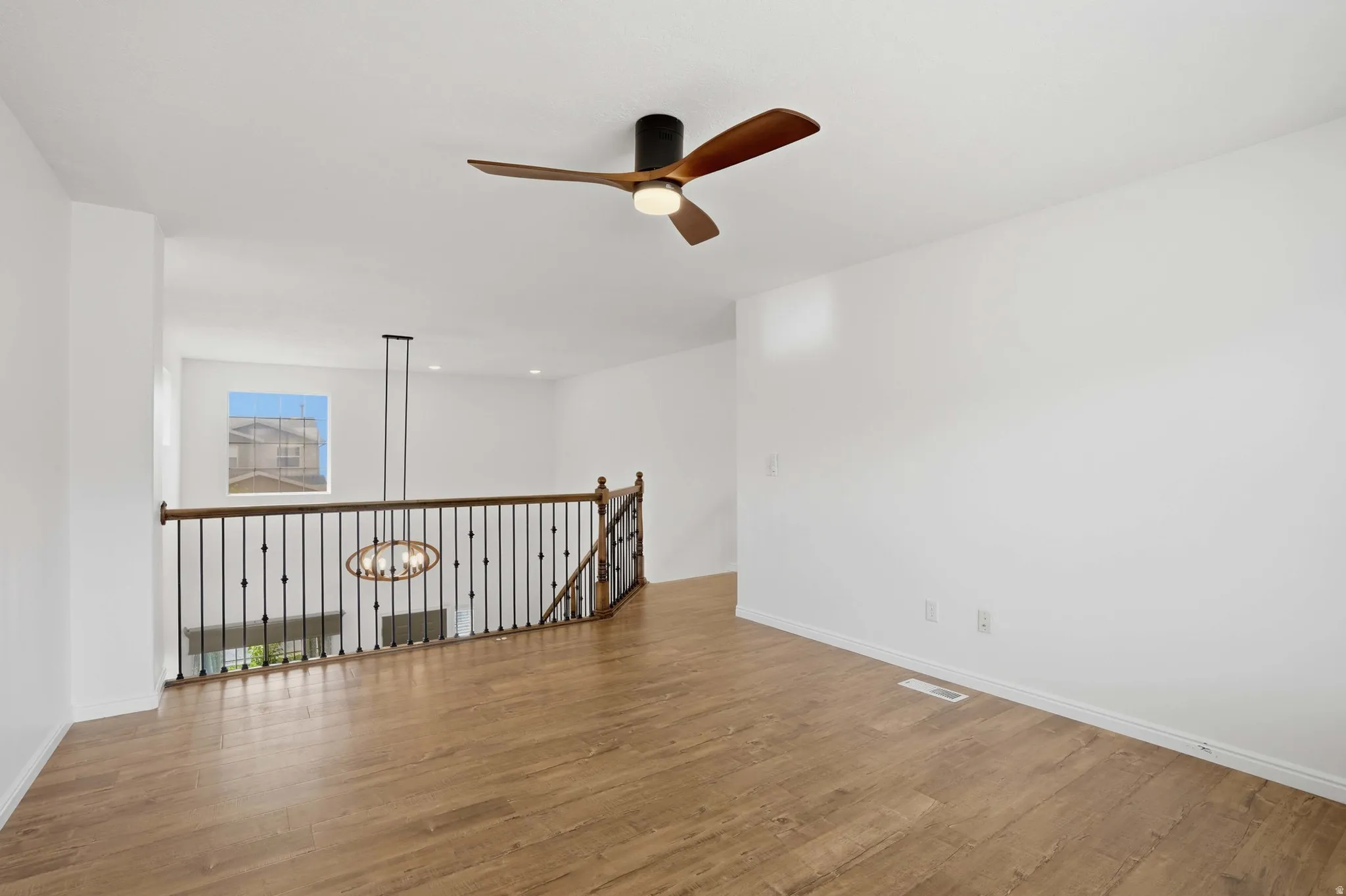 Spacious room featuring wood-finish flooring, a modern ceiling fan, and white walls