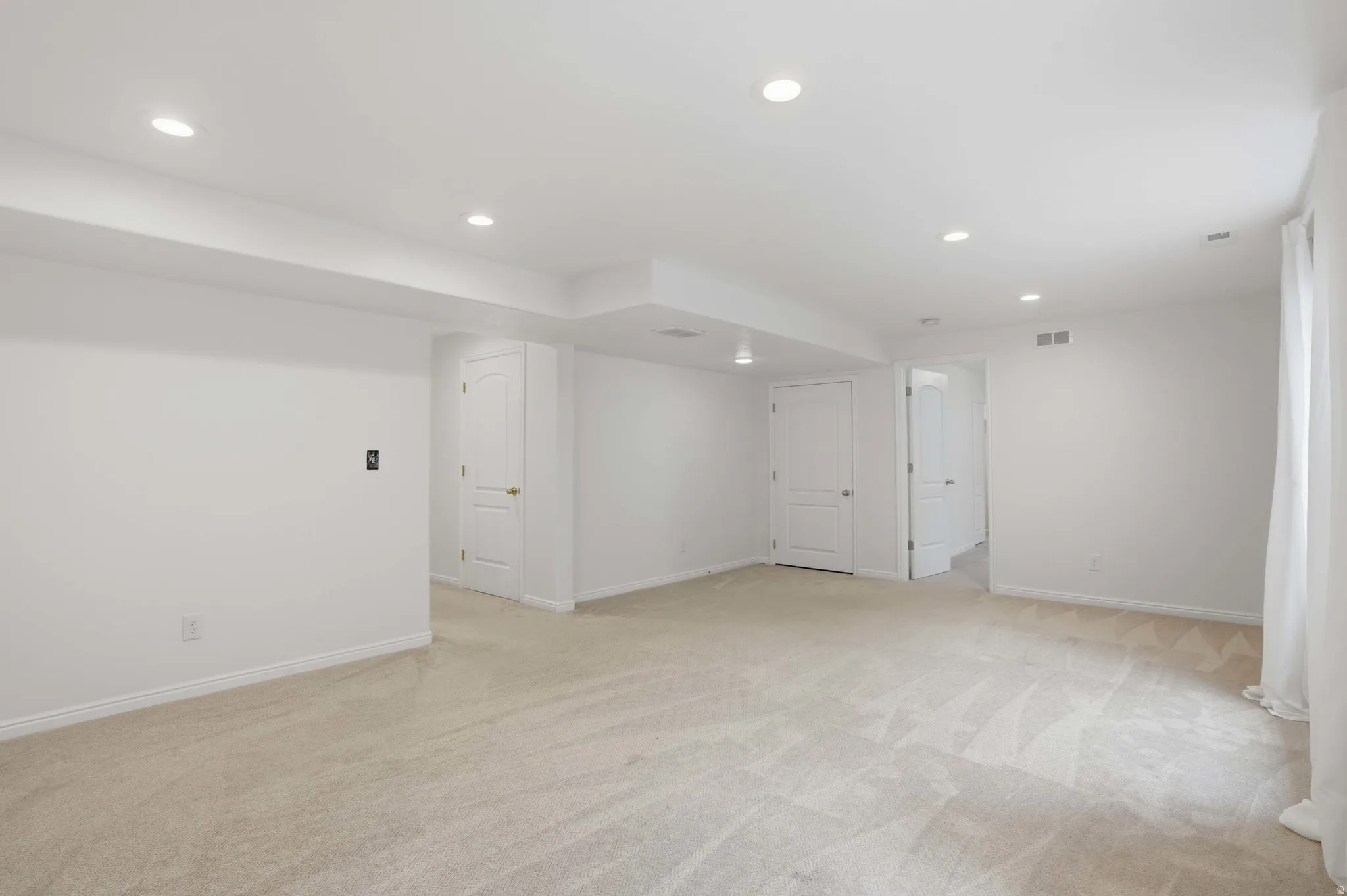 Spacious room featuring neutral carpeting, recessed lighting, white walls, and multiple panel doors