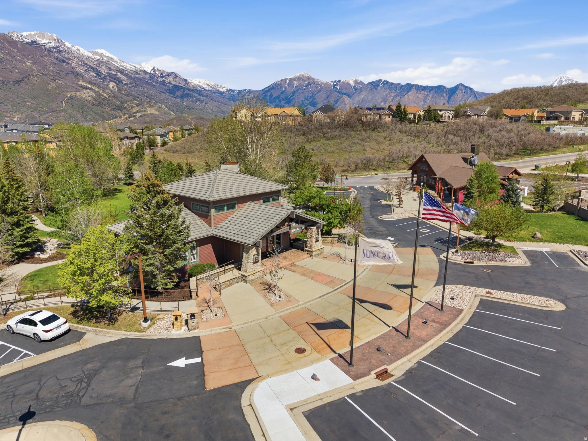 Mountain backdrop featuring a multi-story building with a tile roof, an expansive parking area, paved walkways, and mature landscaping