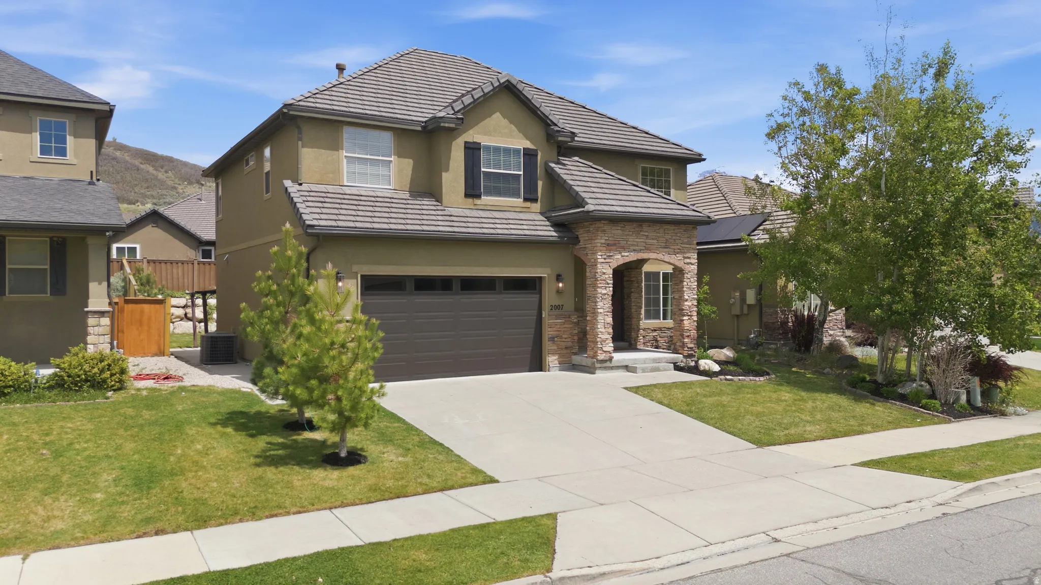Two-story residence featuring a tile roof, stucco exterior, stone archway entry, dark-toned garage door, and a concrete driveway