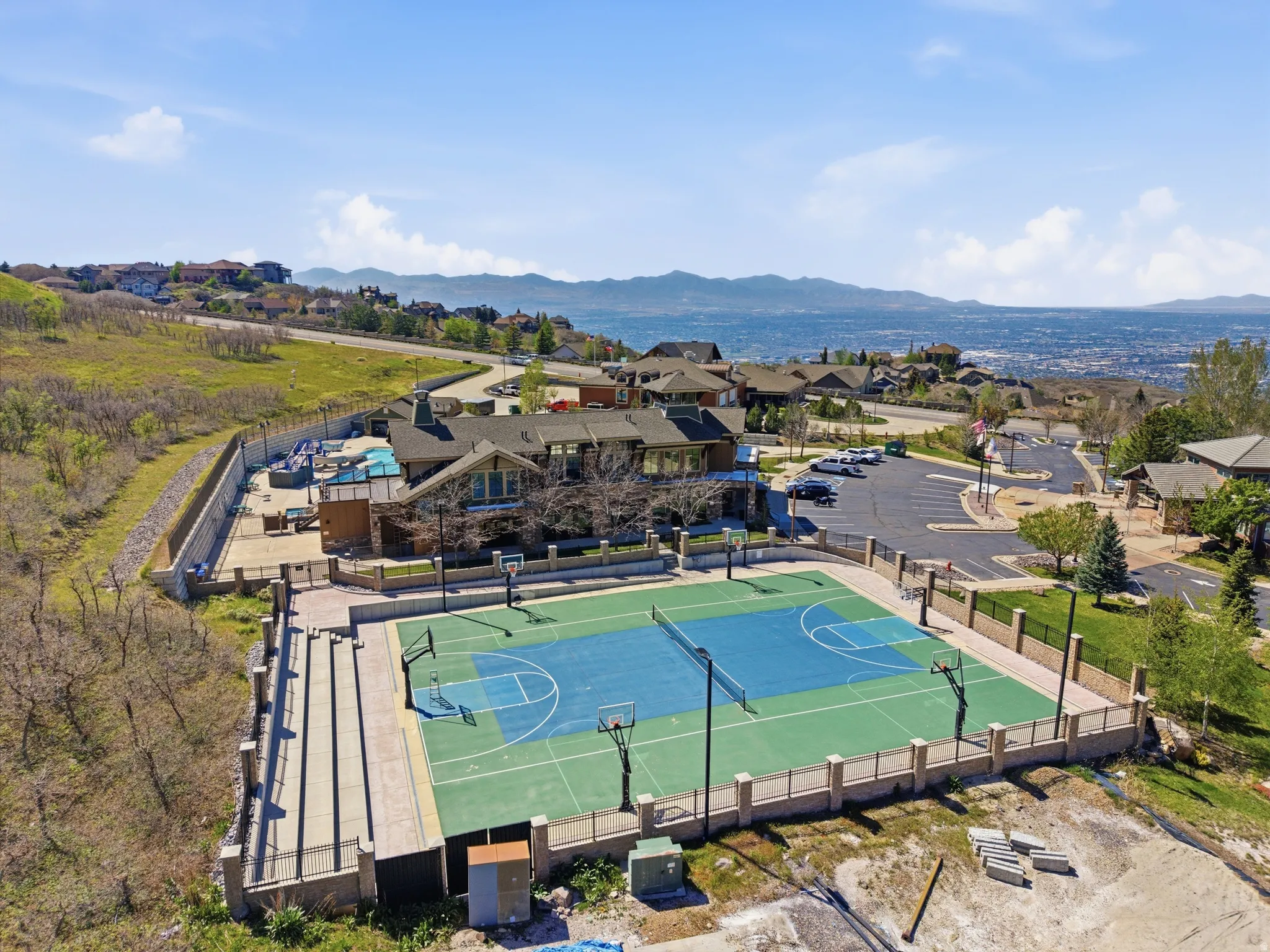 Outdoor recreation area featuring a full-size tennis court with basketball hoops, a swimming pool, and a structured clubhouse