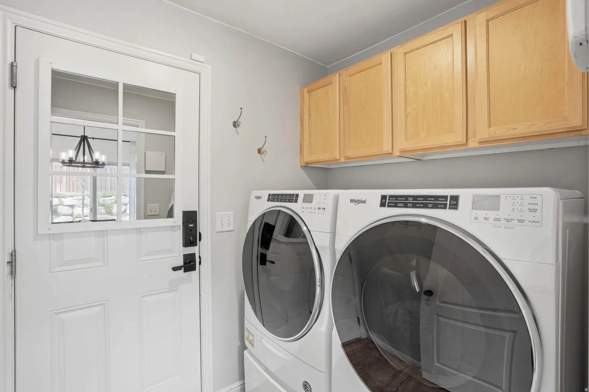 Dedicated laundry area featuring a white paneled door with windowpanes, light wood-finish cabinetry, and wall-mounted hooks