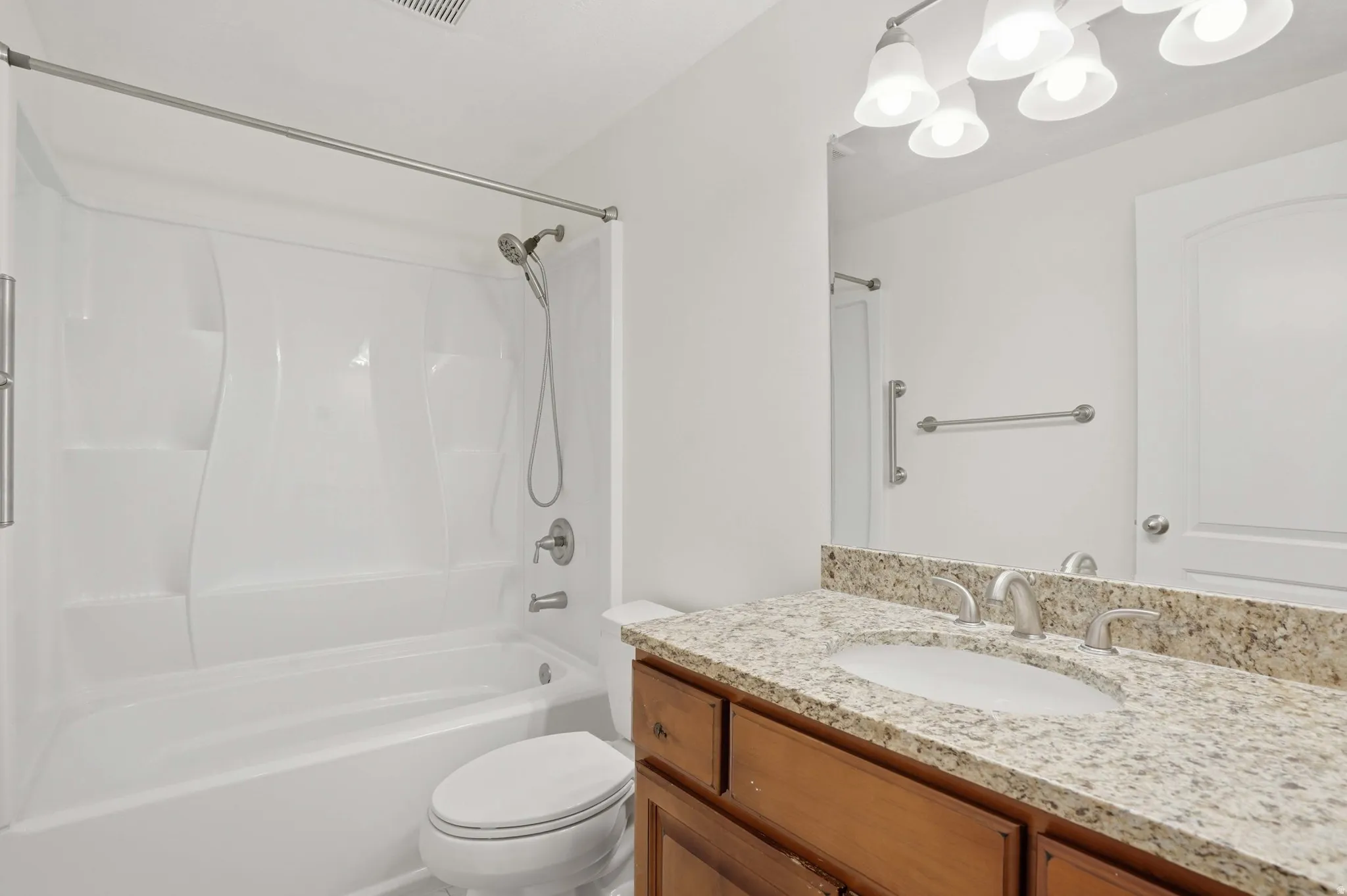 Bathroom featuring a granite-finish vanity with an undermount sink and brushed nickel faucet, a fiberglass tub/shower combination with a handheld showerhead, and a multi-bulb vanity light fixture