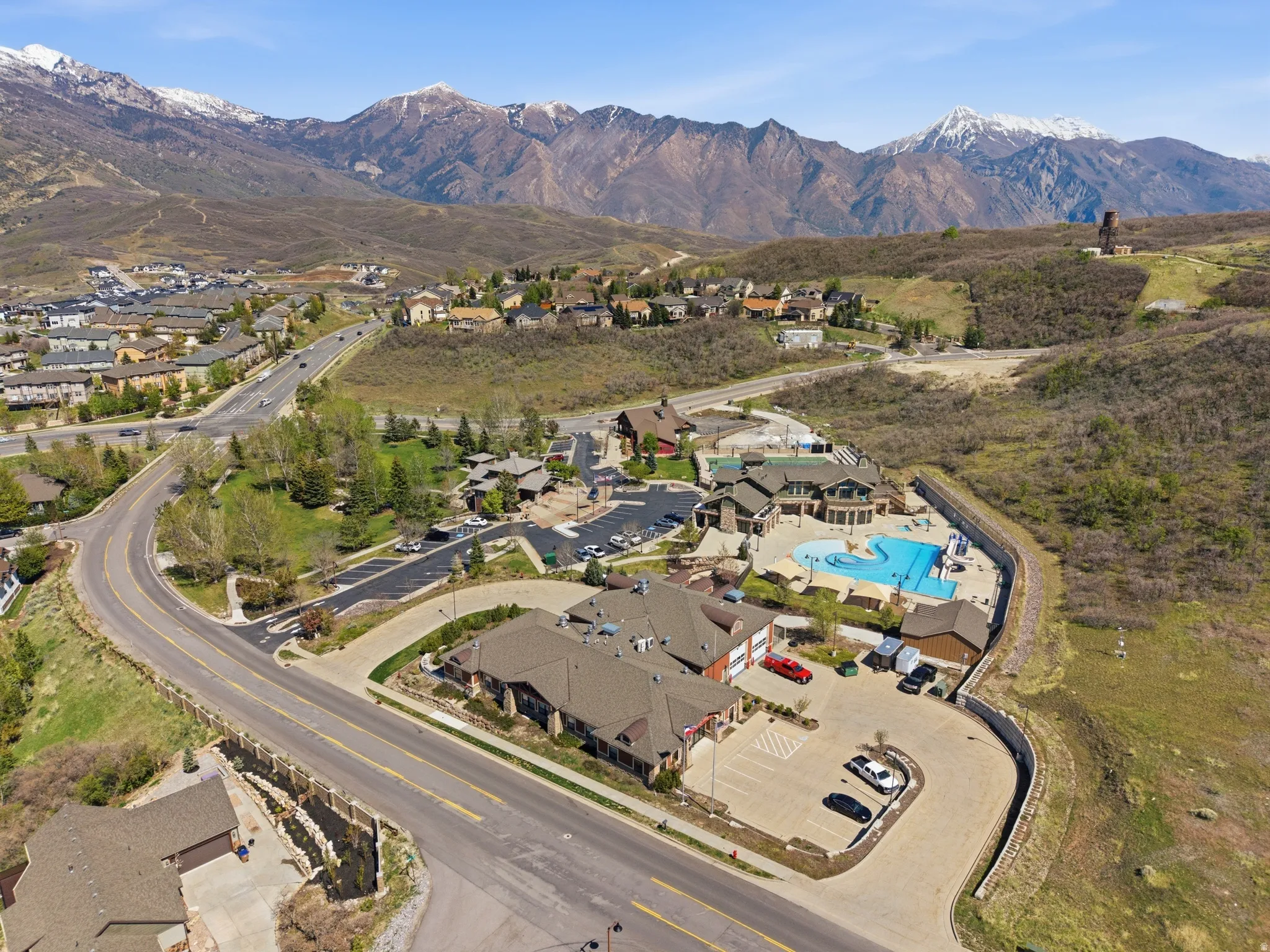 Expansive community amenities featuring multiple buildings with gabled roofs, a large outdoor swimming pool, and a winding road system