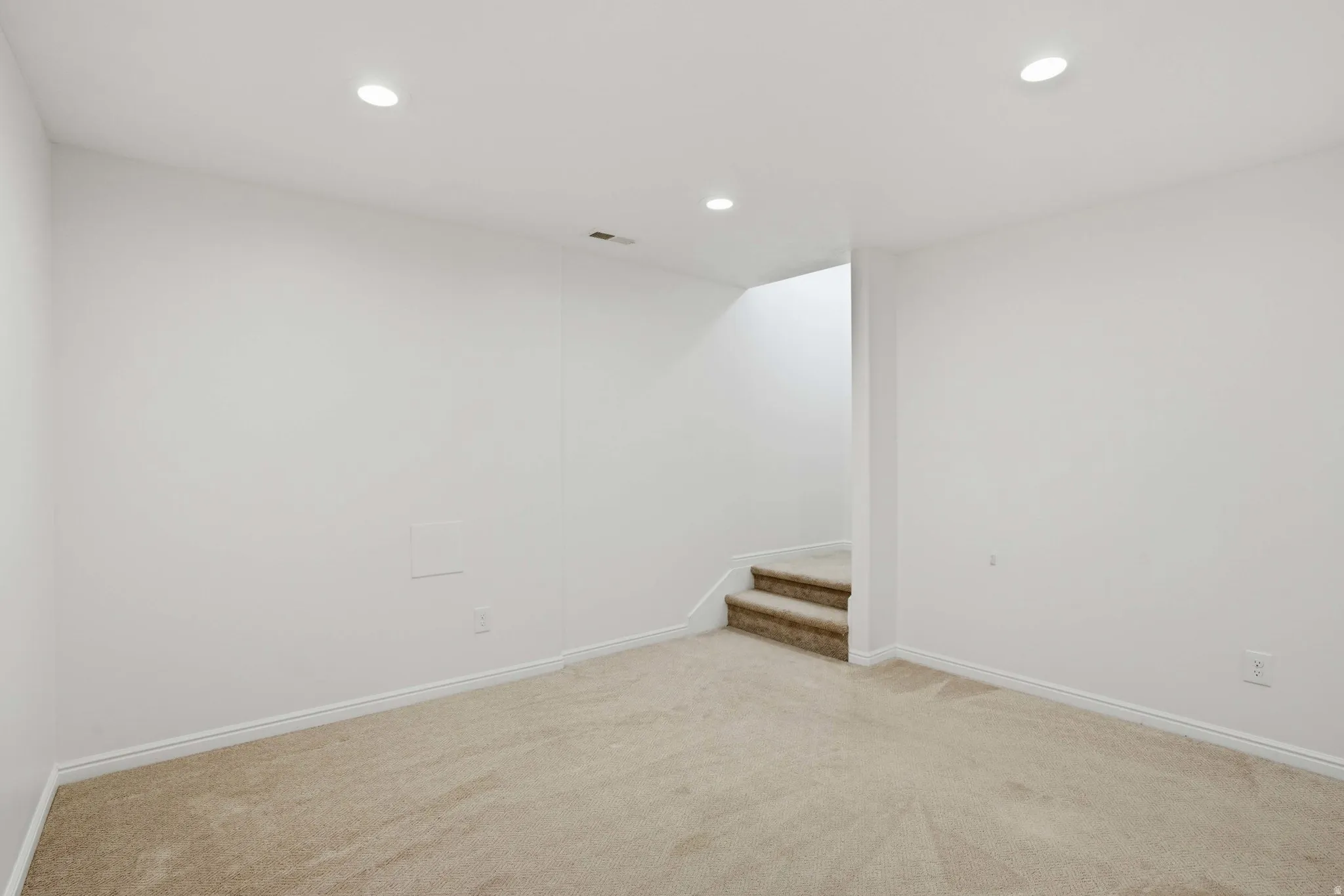 Carpeted room featuring recessed lighting, light-toned walls, white baseboards, and a carpeted staircase