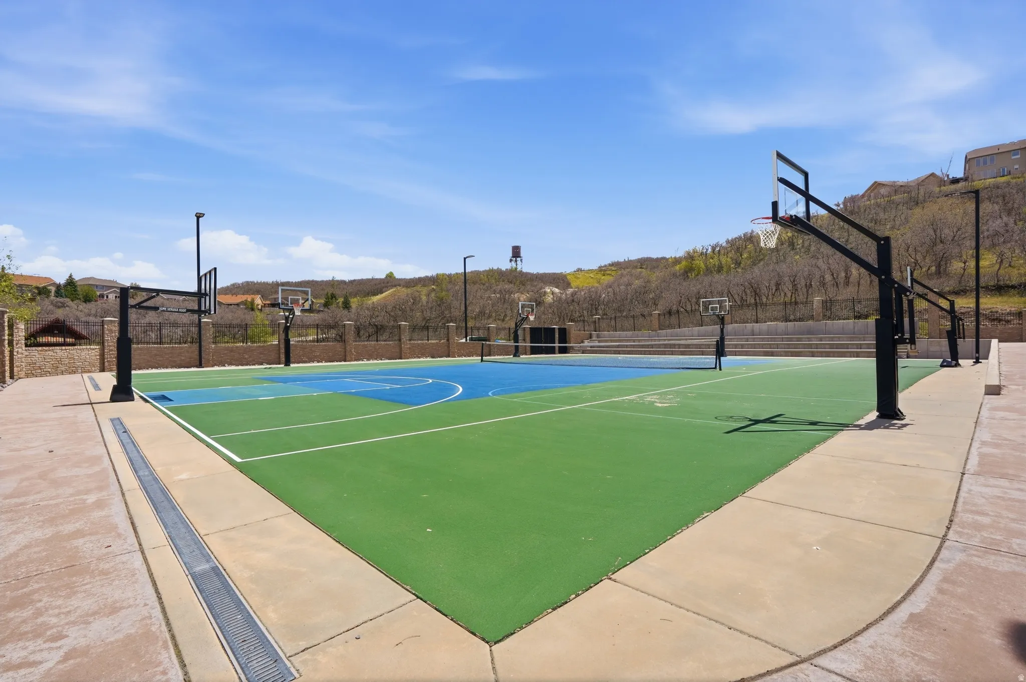 Multi-sport court featuring green and blue surfacing, multiple basketball hoops, and a tennis net
