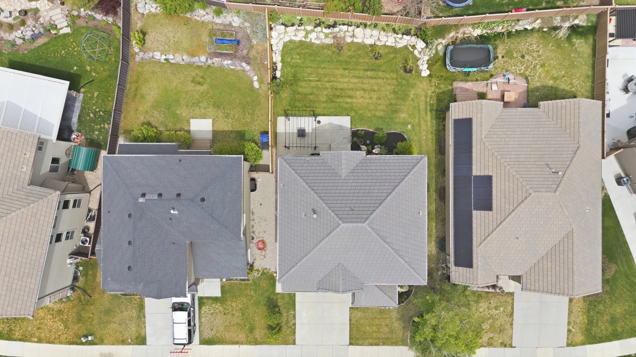 Aerial perspective showcasing a property with a grey shingle roof, a paved driveway, and a fenced backyard featuring a grassy lawn