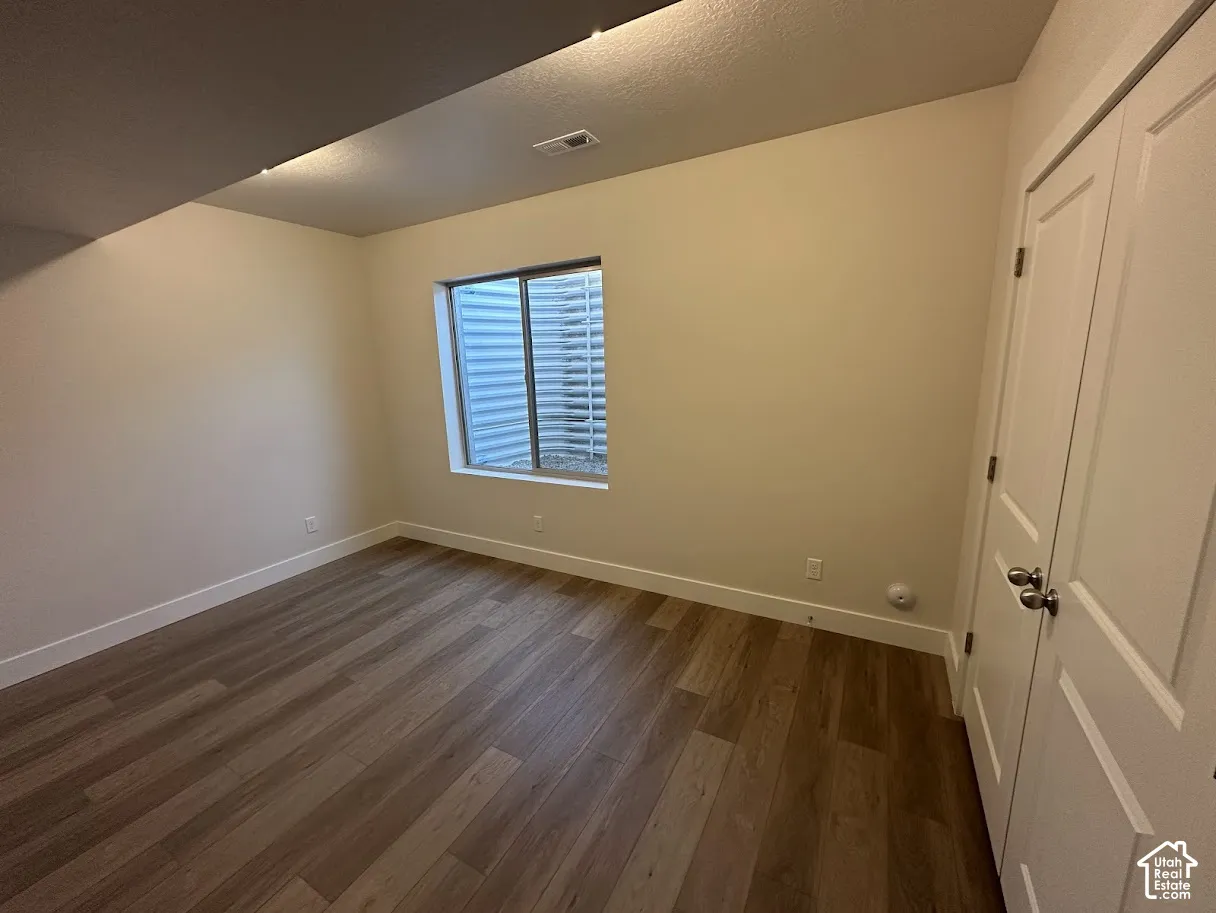 Room featuring wood-finish flooring, a window with a metal window well, light-toned wall paint, and a double-door closet with brushed nickel hardware,Picture taken from comparable unit.