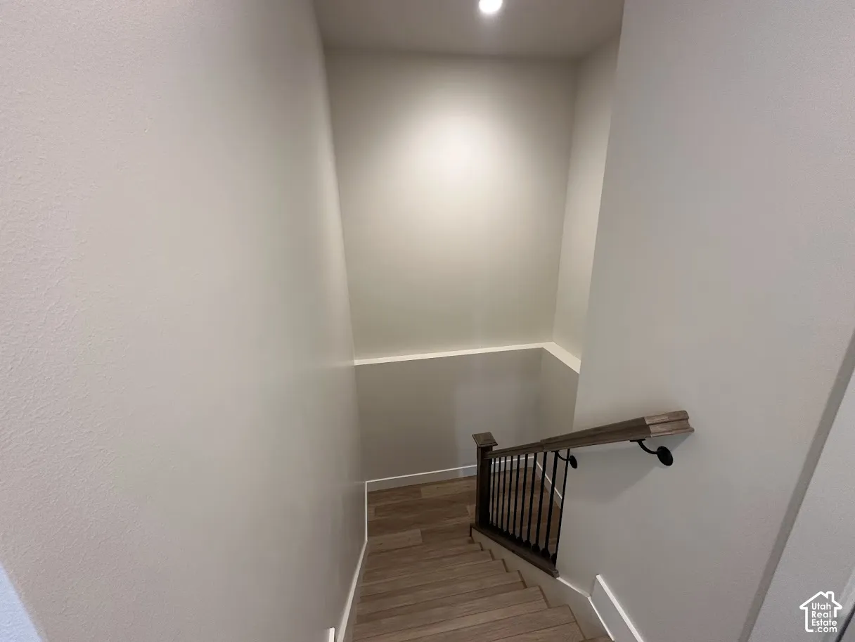 Stairway featuring wood-finish treads, a dark wood-finish handrail, black metal balusters, and recessed lighting.Picture taken from comparable unit.
