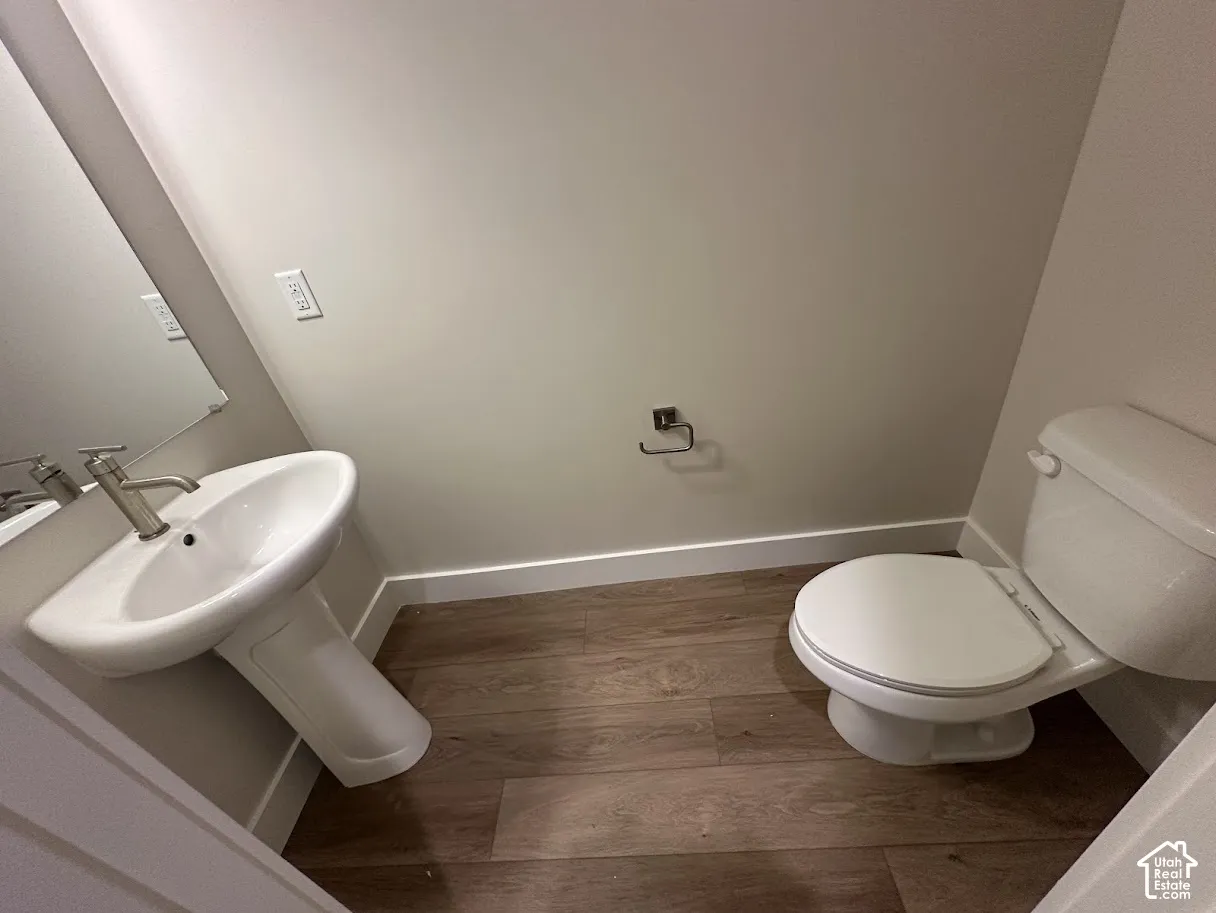 Pedestal sink with a brushed nickel faucet, large wall mirror, white toilet, and wood-finish flooring.Picture taken from comparable unit.