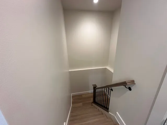 Stairway featuring wood-finish treads, a dark wood-finish handrail, black metal balusters, and recessed lighting