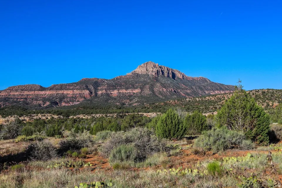 Expansive natural landscape featuring a prominent mountain range with visible rock layers and dense vegetation at its base