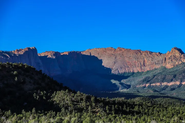 Expansive mountain backdrop featuring rugged red rock formations, verdant lower slopes, and a clear blue sky