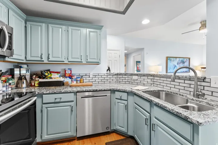 Kitchen featuring light blue cabinetry, stainless steel appliances, a double basin sink with gooseneck faucet, light-toned granite countertops, and a subway tile backsplash