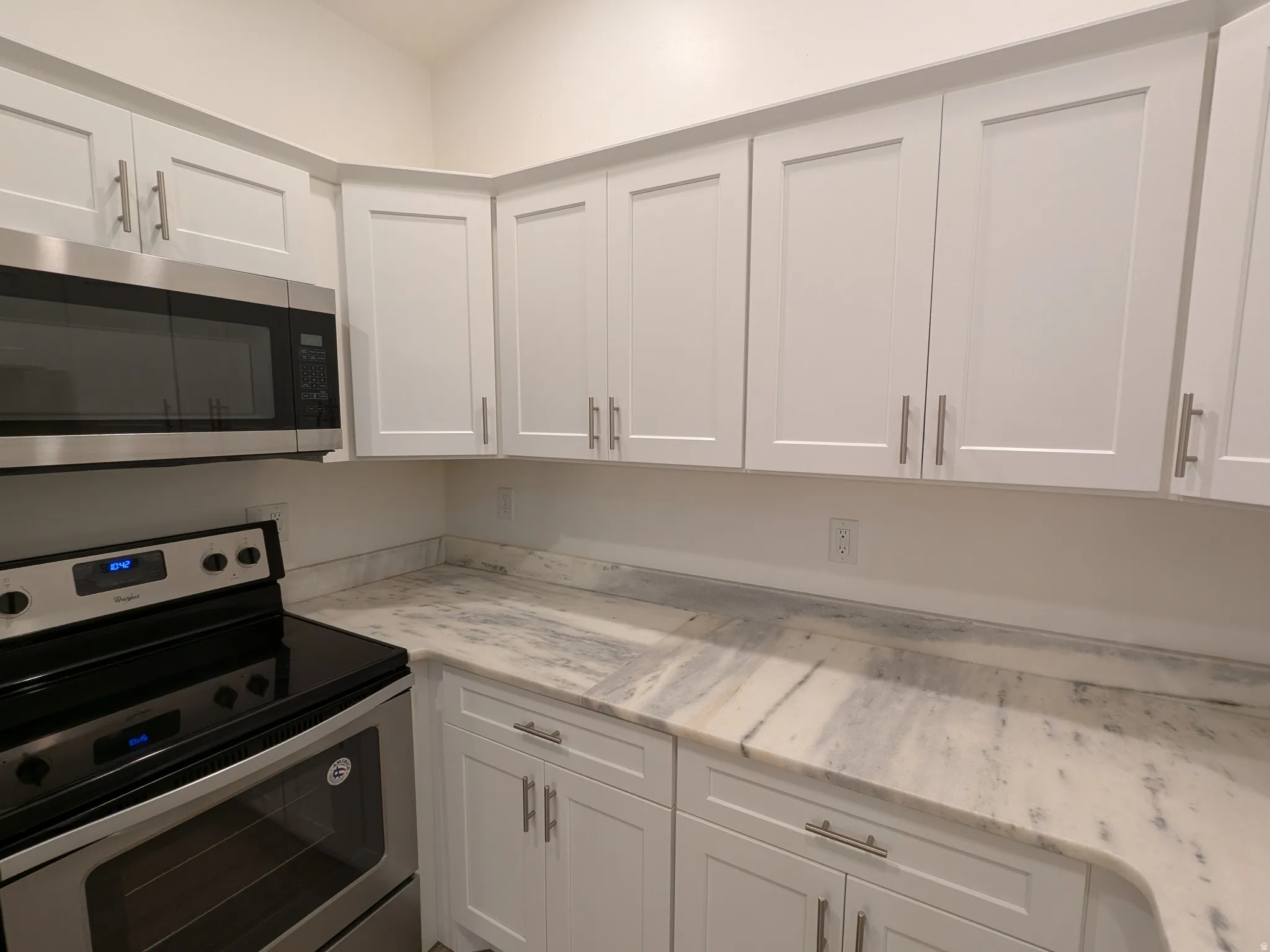 Kitchen featuring stainless steel appliances, white cabinets, and light stone countertops