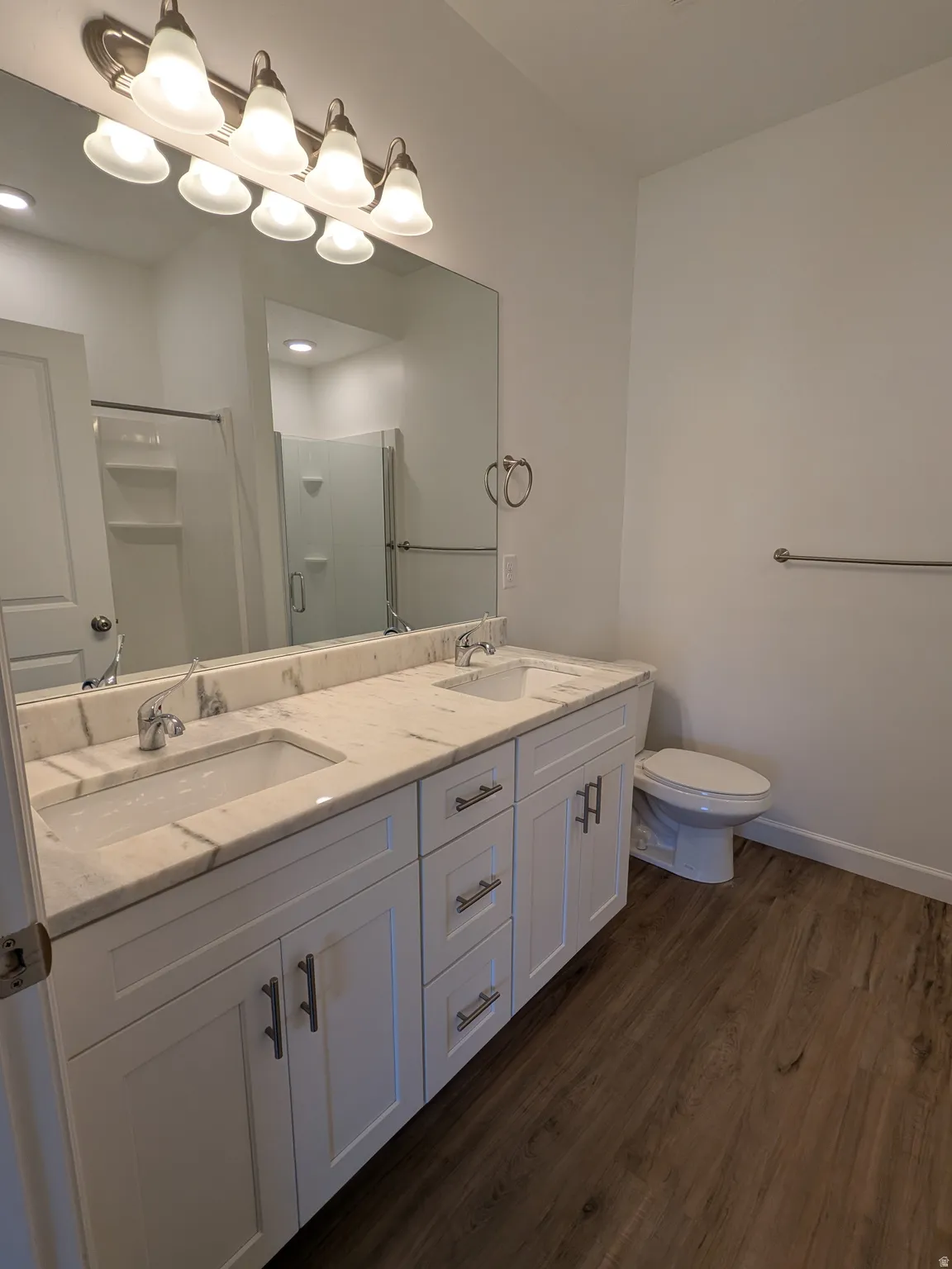 Bathroom with double vanity, a stall shower, and dark wood-type flooring