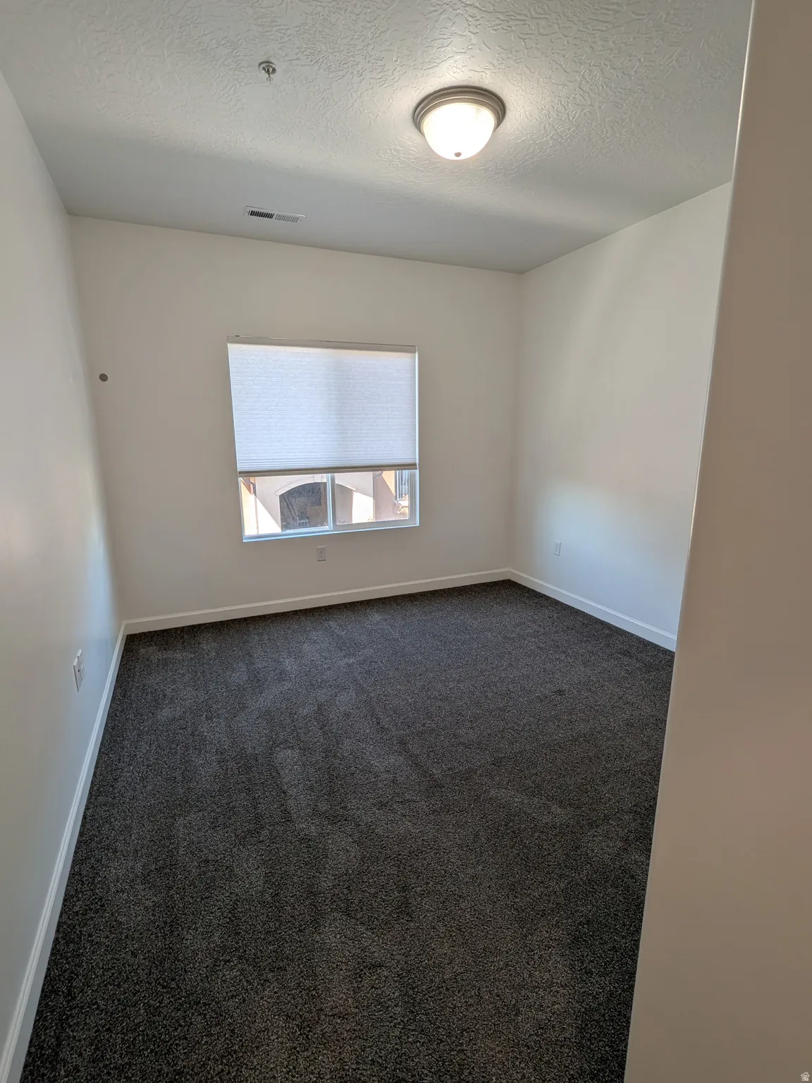 Empty room with dark colored carpet and a textured ceiling