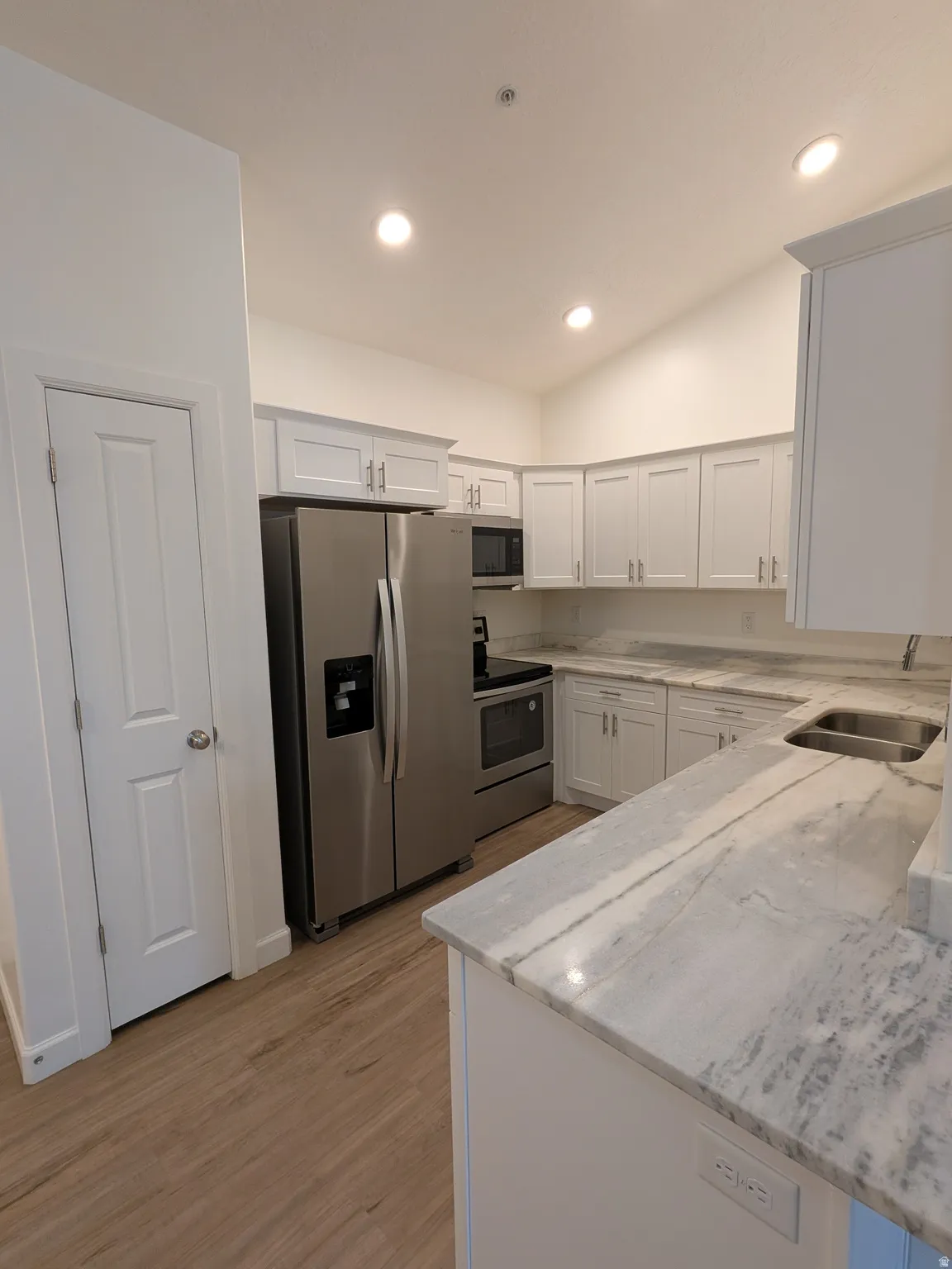 Kitchen featuring stainless steel appliances, light wood-type flooring, light stone counters, white cabinets, and recessed lighting