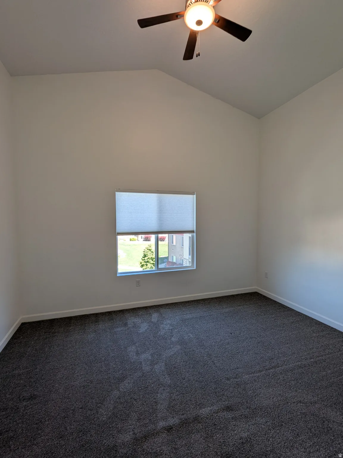 Empty room with dark carpet, a ceiling fan, and lofted ceiling