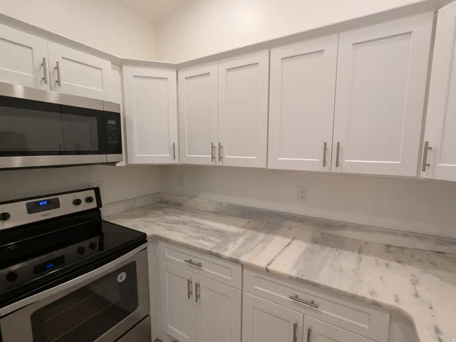 Kitchen featuring stainless steel appliances, white cabinets, and light stone countertops