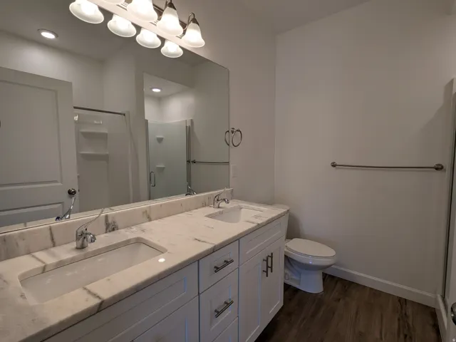 Full bath featuring a shower stall, double vanity, and dark wood finished floors
