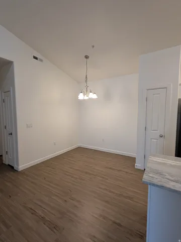 Unfurnished dining area with dark wood-type flooring, suspended lighting, and lofted ceiling