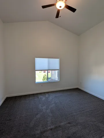 Empty room with dark carpet, a ceiling fan, and lofted ceiling