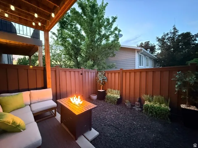 Private outdoor patio featuring a wood ceiling with integrated lighting, a built-in fire pit, and a dark mulch ground cover