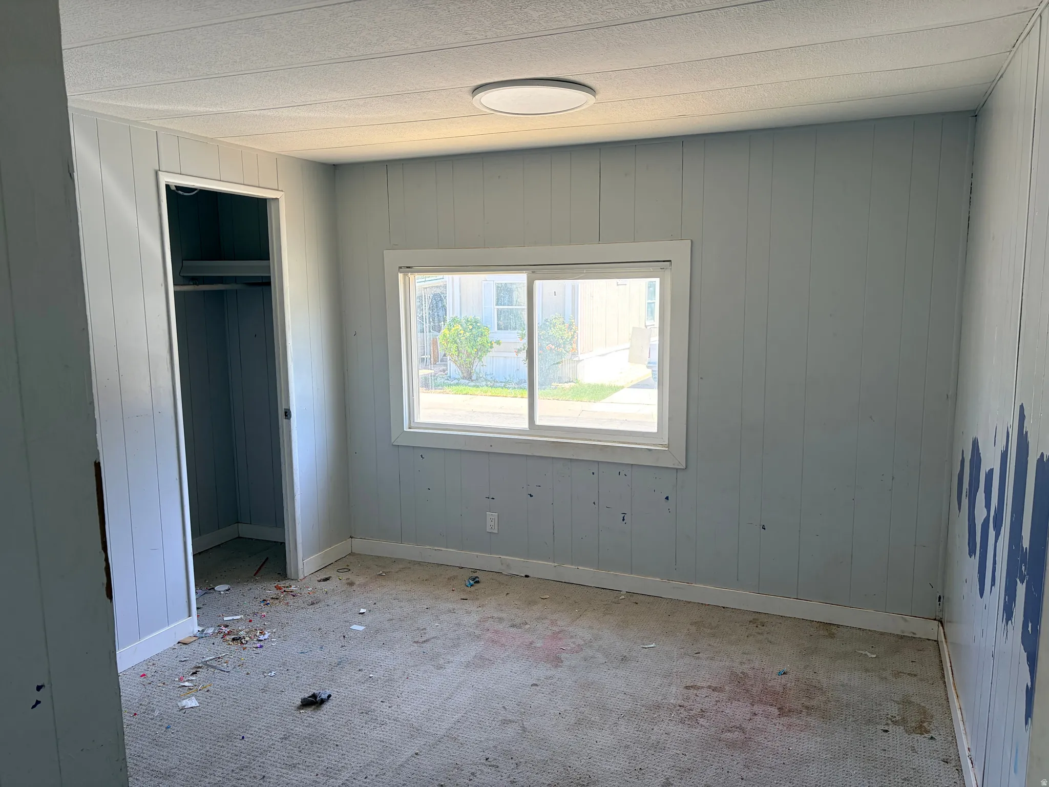 Room featuring a white-framed window, light-colored vertical paneling, and a flush-mount ceiling light