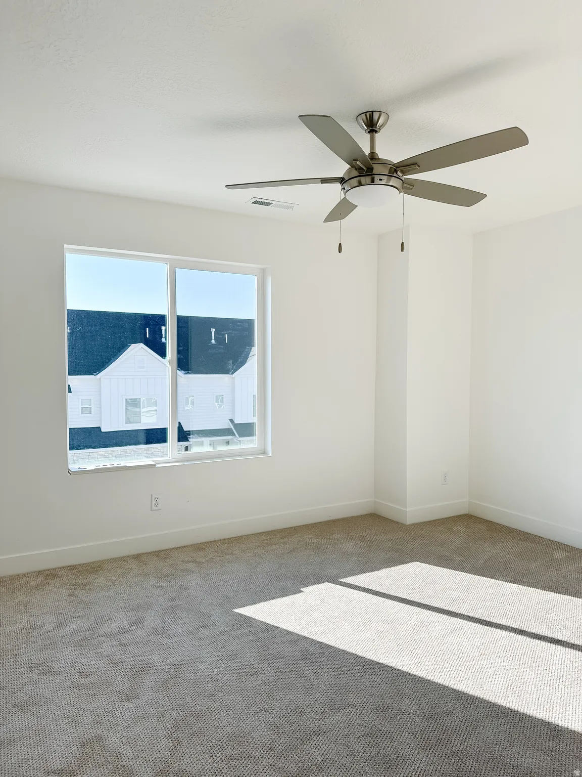Spacious room featuring neutral carpeting, white walls, and a contemporary ceiling fan with integrated lighting