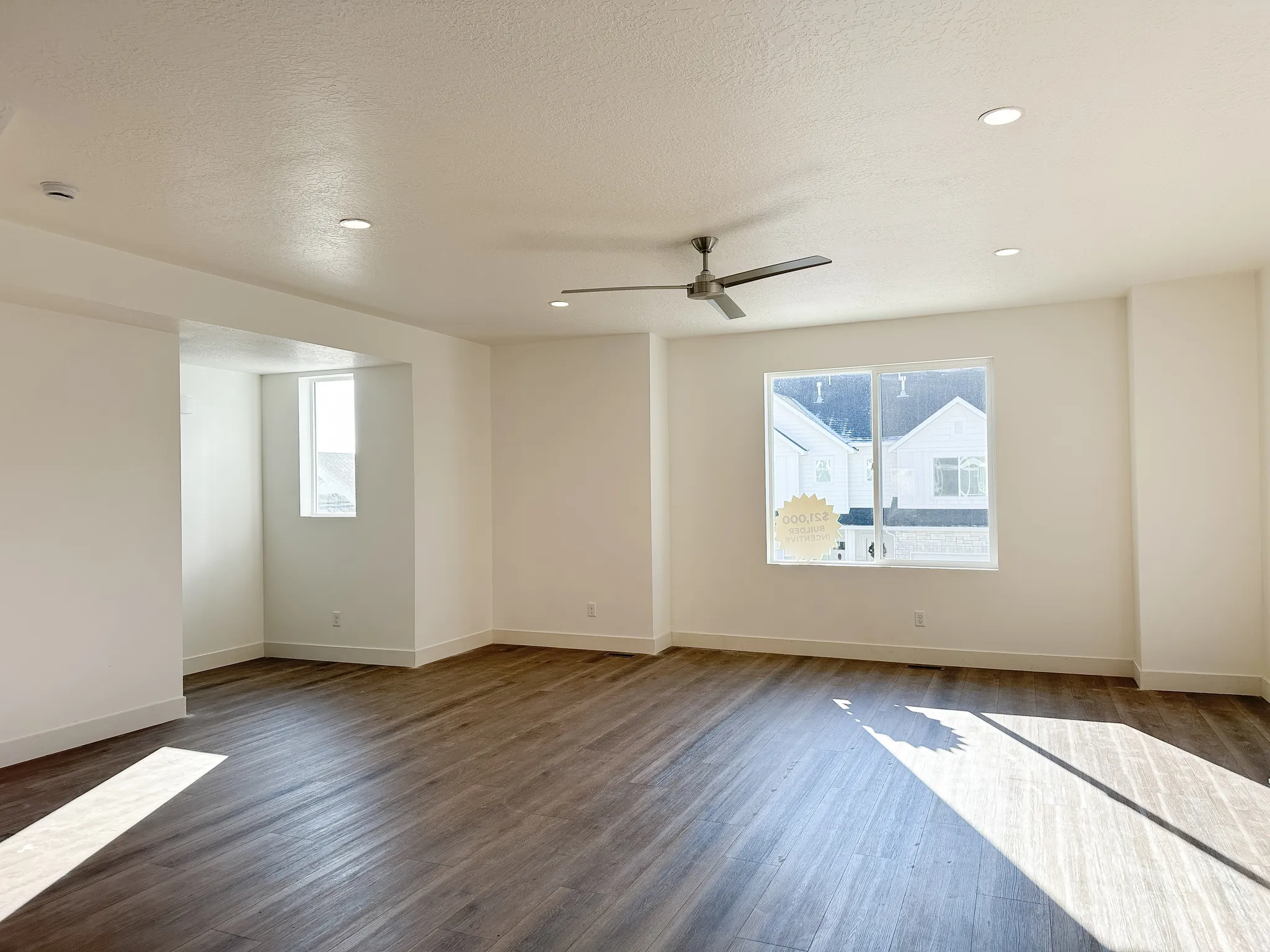 Spacious room featuring wood-finish flooring, recessed lighting, a modern ceiling fan, and multiple windows with white trim