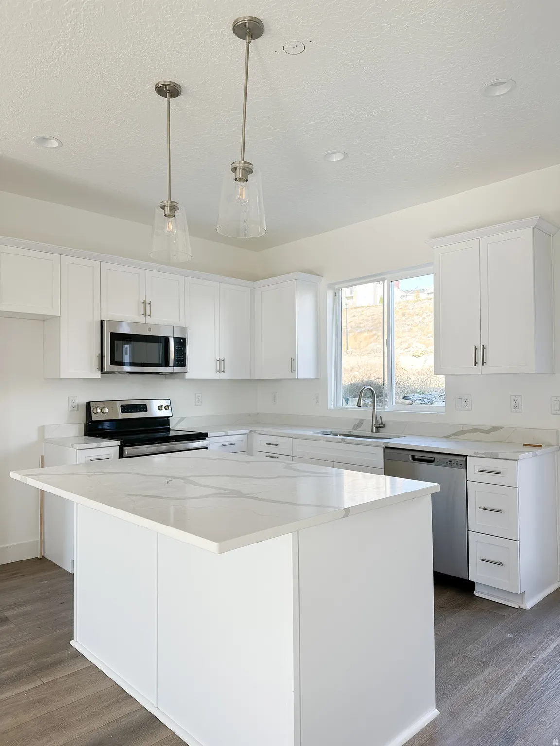 Bright kitchen featuring a central island with a white patterned countertop, white cabinetry with silver hardware, and stainless steel appliances