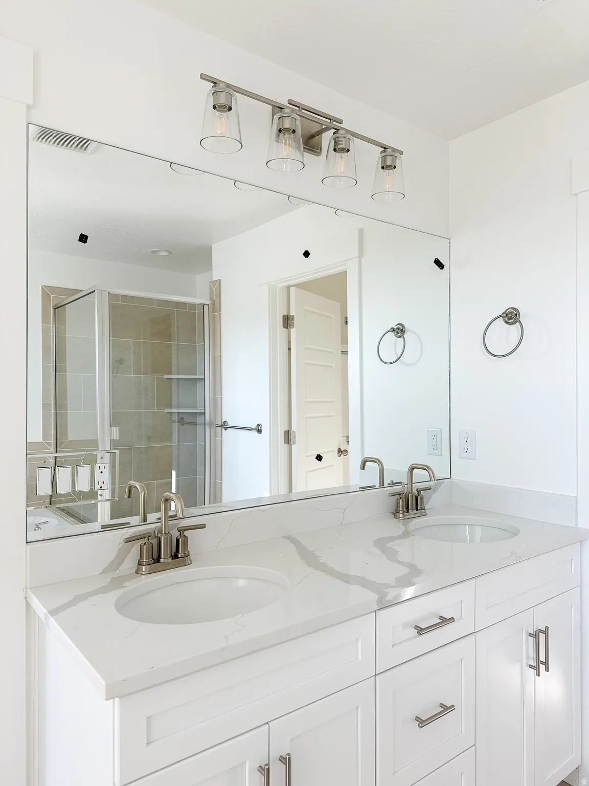 Dual vanity featuring white shaker-style cabinetry, a stone-finish countertop with integrated sinks, and brushed nickel hardware