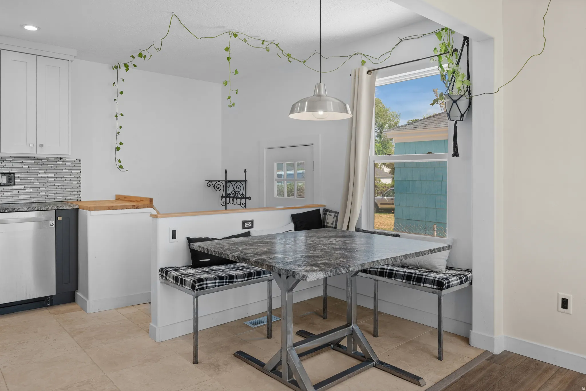 Kitchen dining area featuring a built-in bench, a large window, tile flooring, a pendant light fixture, and a partial view of kitchen cabinetry with a mosaic tile backsplash