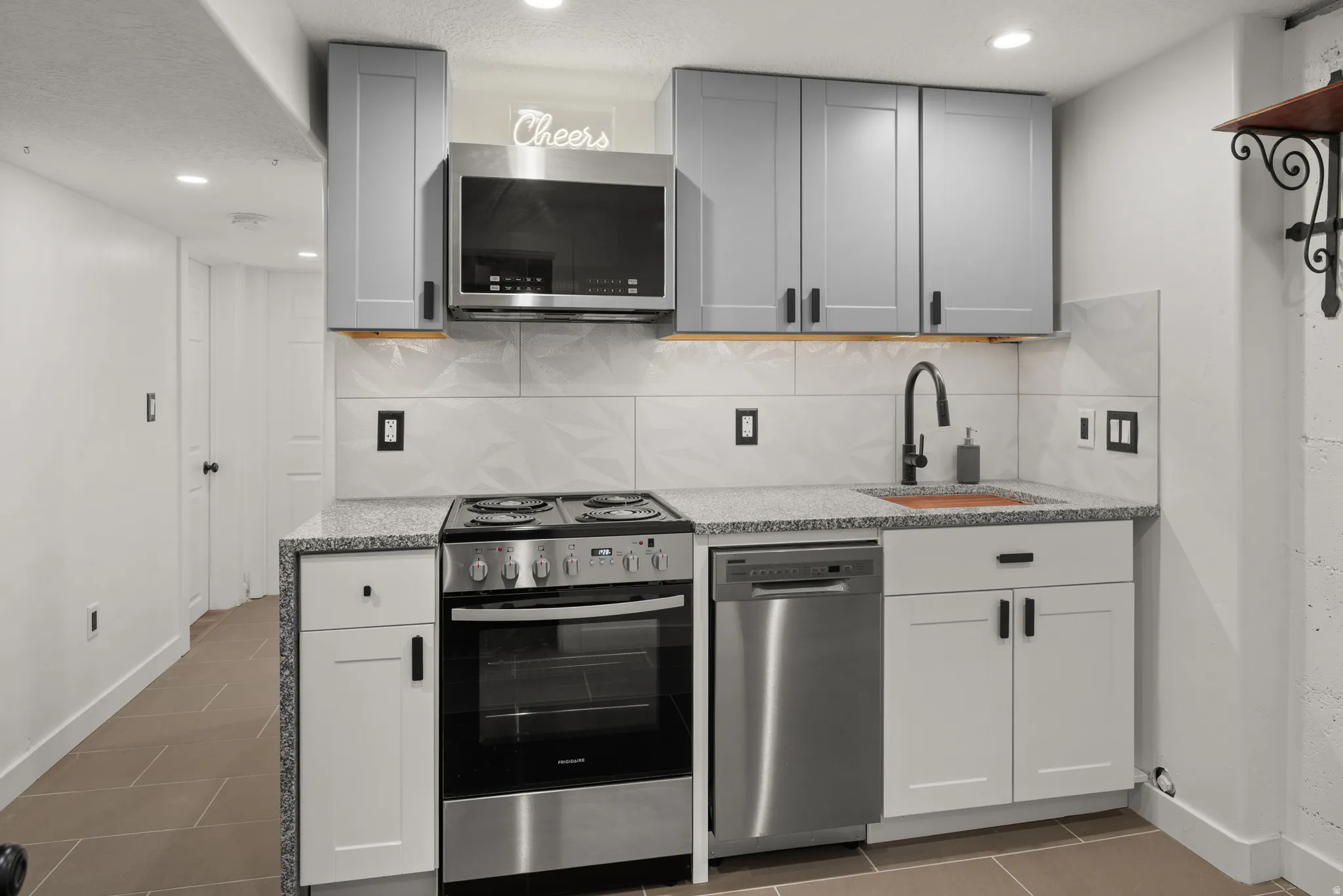 Modern kitchen featuring a stainless steel appliance suite, light grey upper cabinetry, white lower cabinetry, and a stone-finish countertop