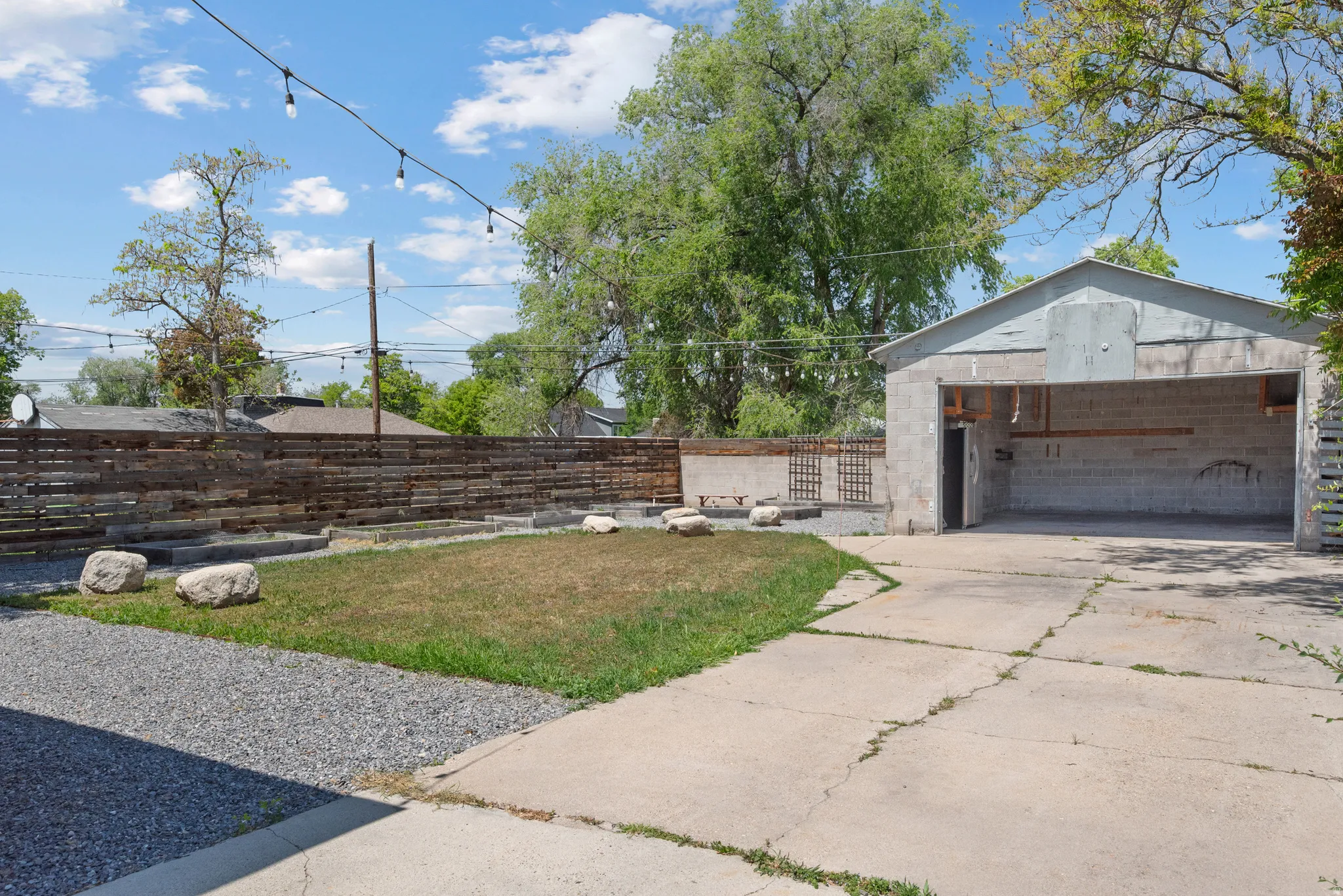 Detached garage featuring a concrete driveway, string lights, a wood fence, and a gravel area