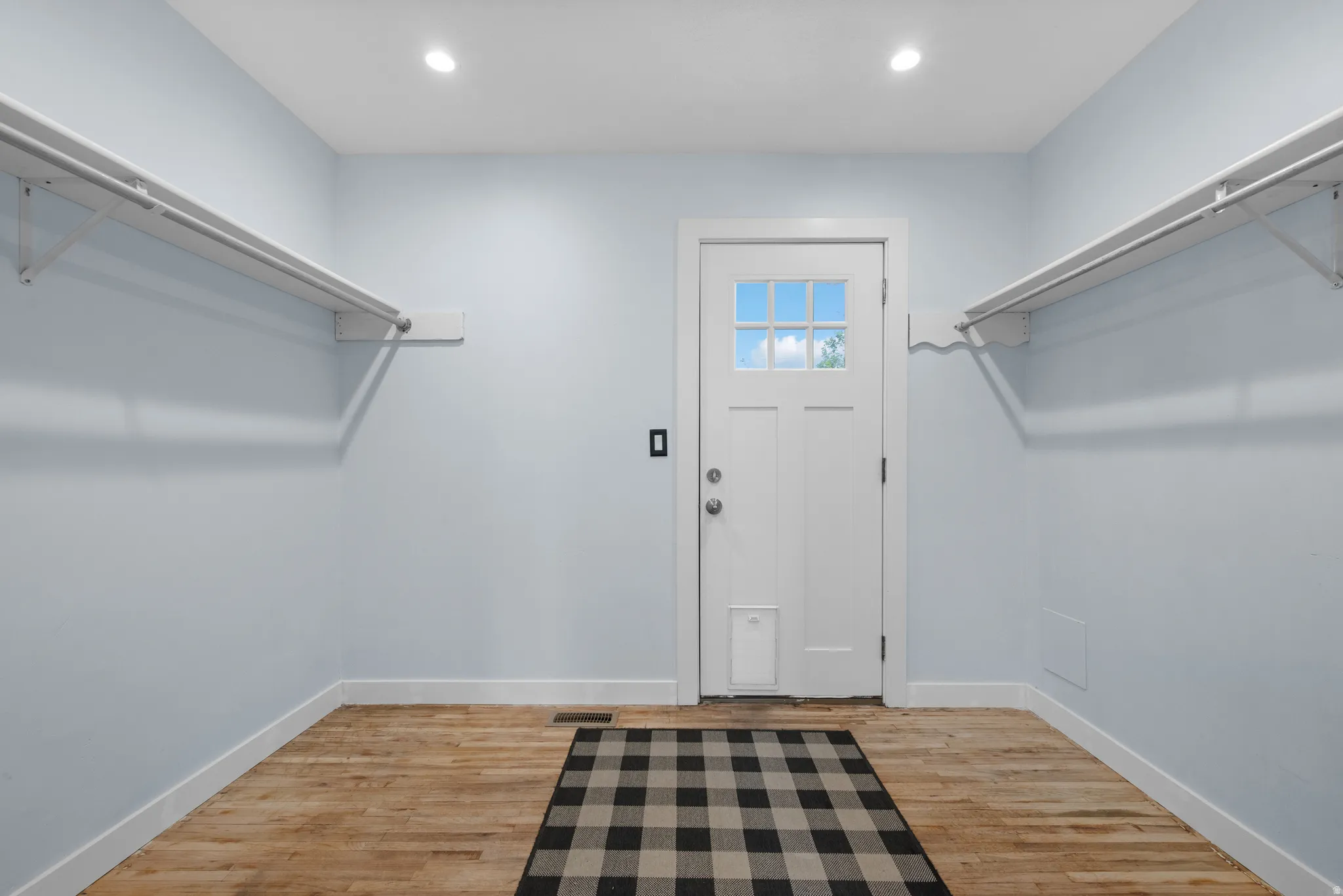 Entryway featuring light blue walls, natural wood-finish flooring, recessed lighting, and a white paneled door with a multi-pane window