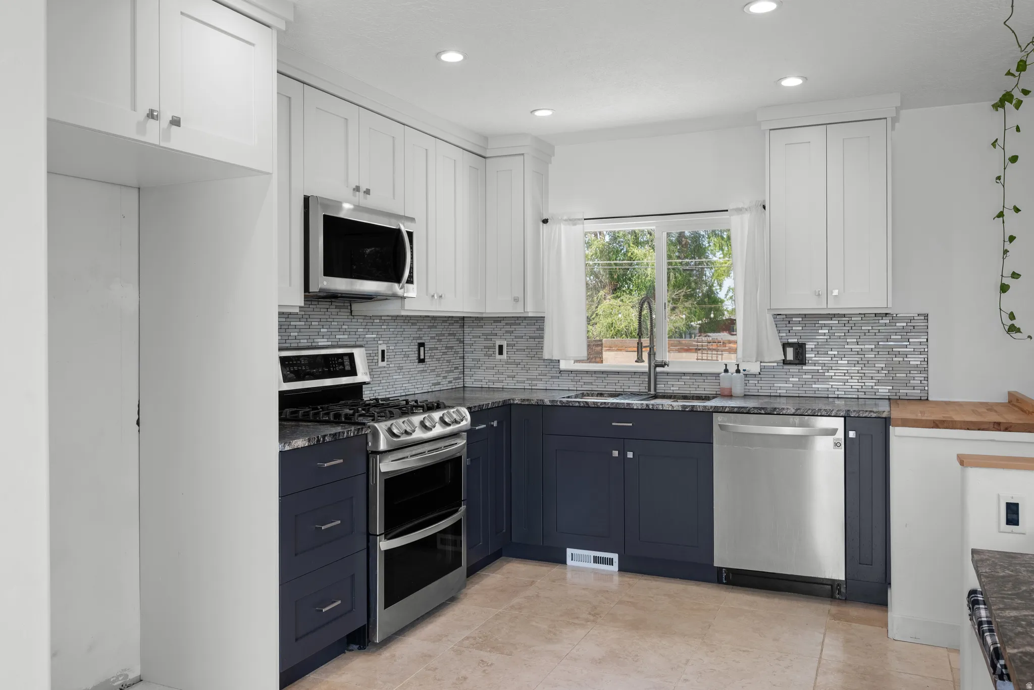 Kitchen featuring two-tone cabinetry with white upper and dark lower cabinets, stainless steel appliances, mosaic tile backsplash, and light-toned tile flooring