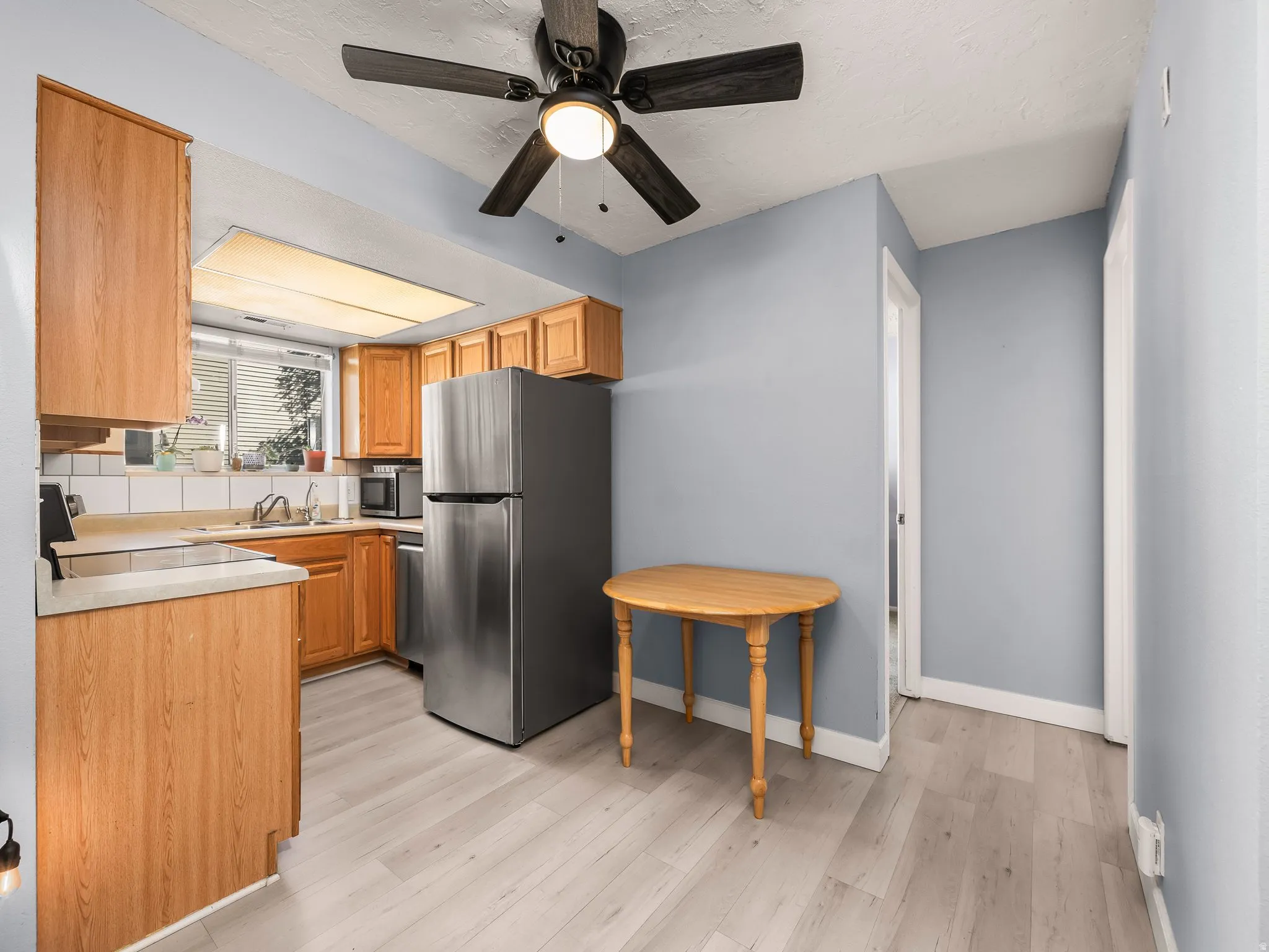 Kitchen featuring light wood-finish cabinetry, a stainless steel refrigerator, white subway tile backsplash, and light wood-finish flooring