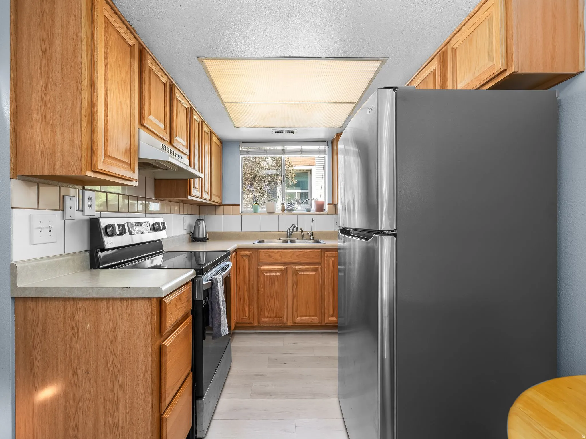 Kitchen featuring light wood cabinetry, light countertops, white tiled backsplash, stainless steel refrigerator, and wood-finish flooring